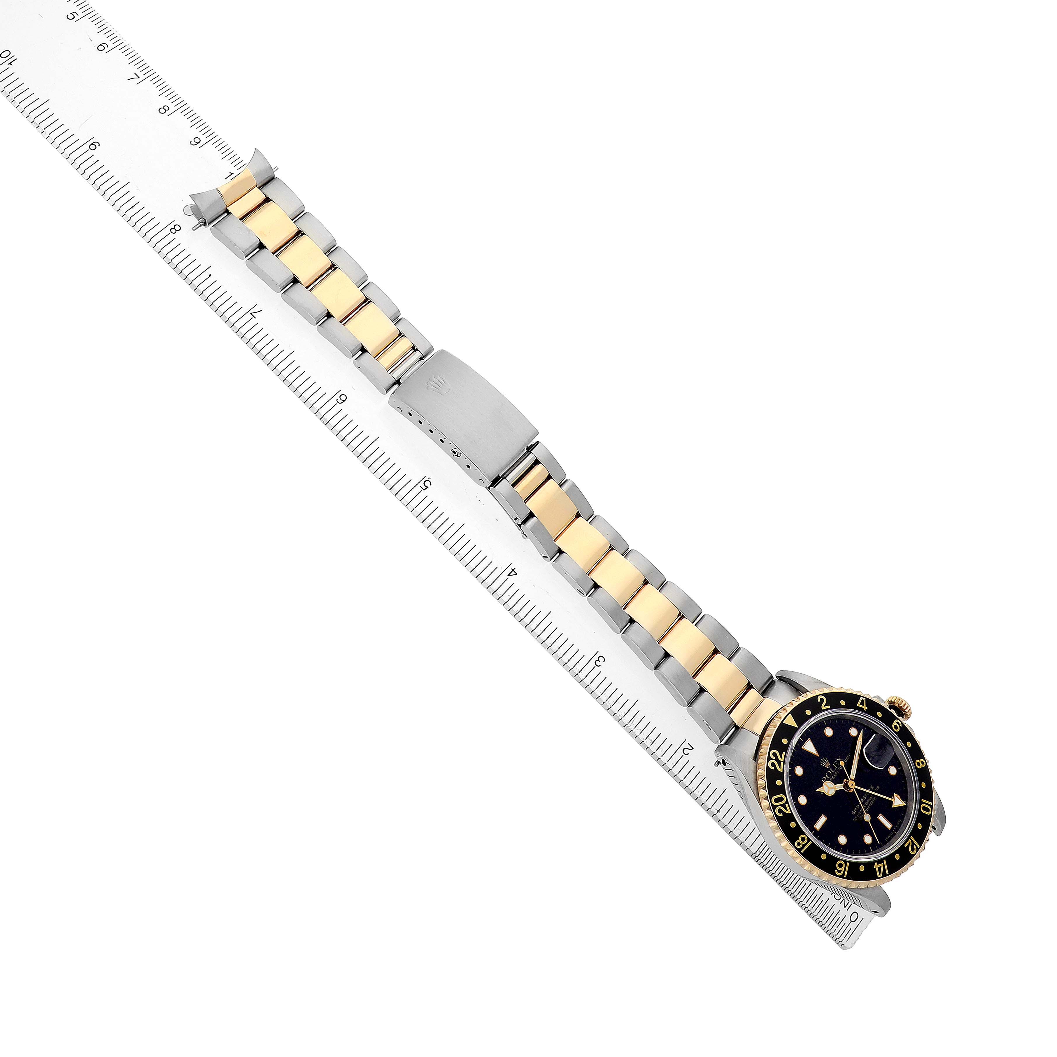 The image shows a Rolex GMT-Master 16713 Men's Steel and Gold (two tone) Black Dial watch with a two-tone bracelet, clasp, and bezel, viewed from above alongside a ruler.