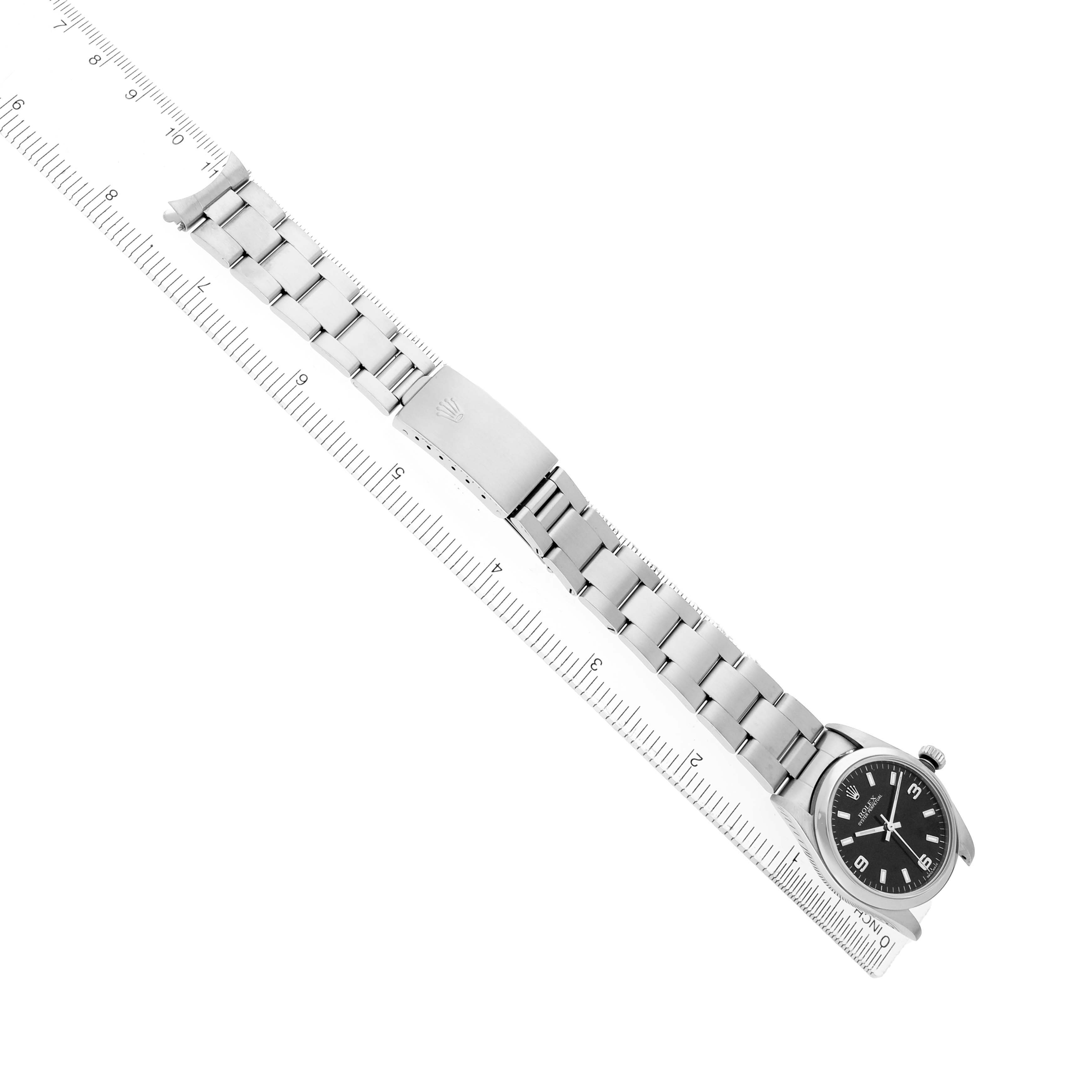 The Rolex Mid-Size 77080 Women's Stainless Steel Black Dial model watch is shown from a top-down angle, highlighting the bracelet, clasp, and watch face alongside a ruler.