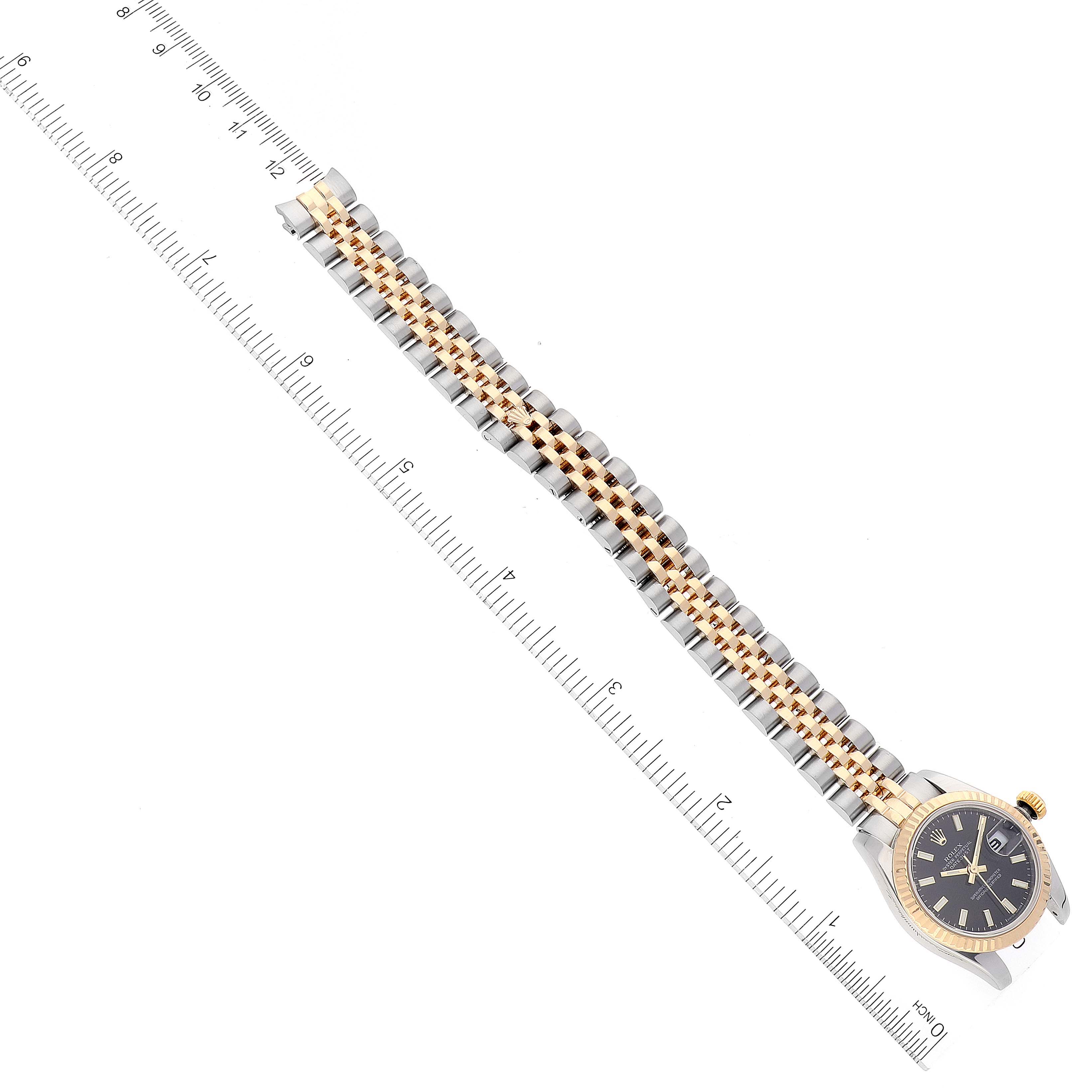 The image shows a Rolex Datejust 179173 Women's Steel and Gold (two tone) Black Dial 179173 Women's Steel and Gold (two tone) Black Dial watch displayed diagonally, highlighting the bracelet and partially the dial, alongside a measuring ruler.