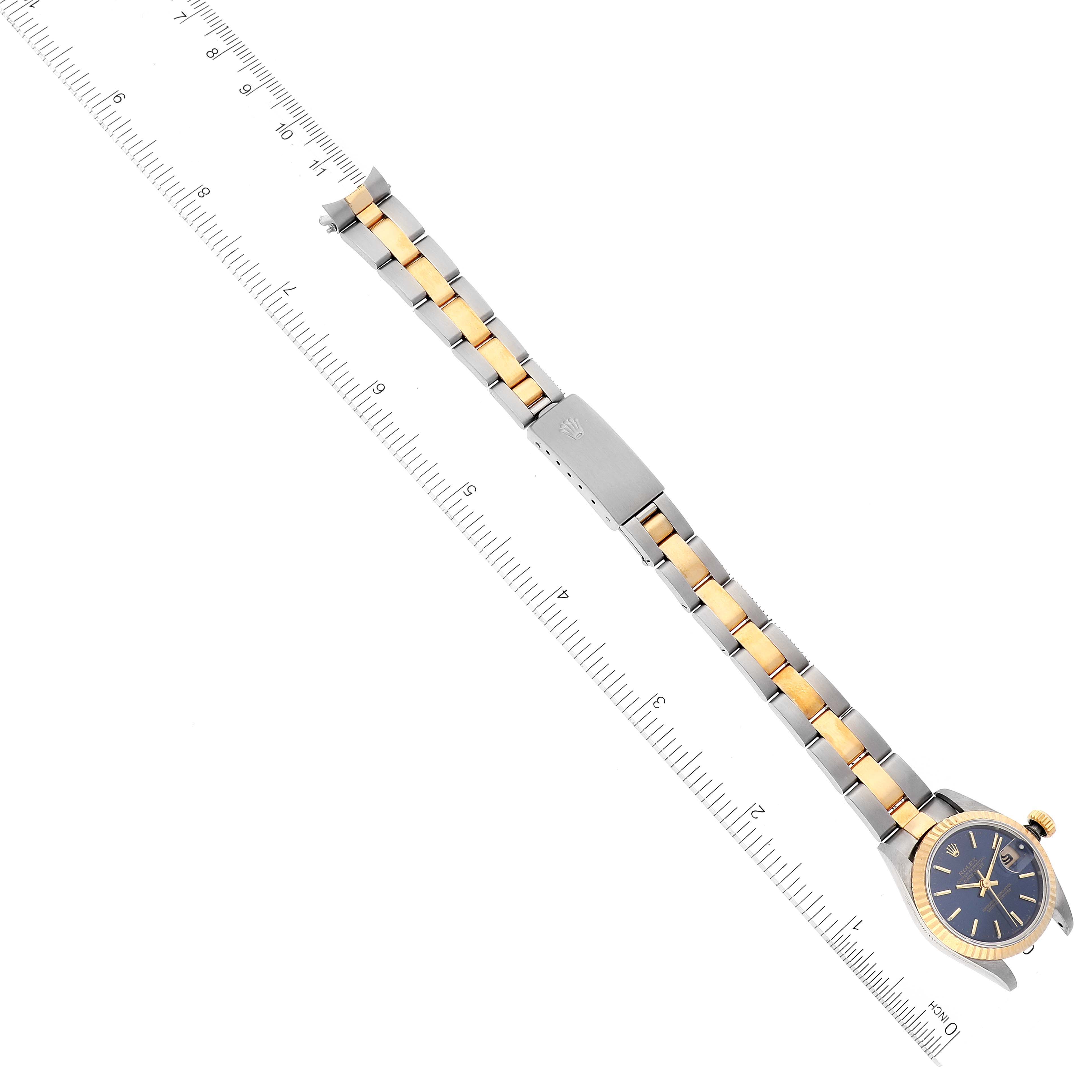 This image shows a top view of a Rolex Datejust 69173 Women's Steel and Gold (two tone) Blue Dial 69173 Women's Steel and Gold (two tone) Blue Dial watch with a two-tone bracelet alongside a ruler measuring its length.