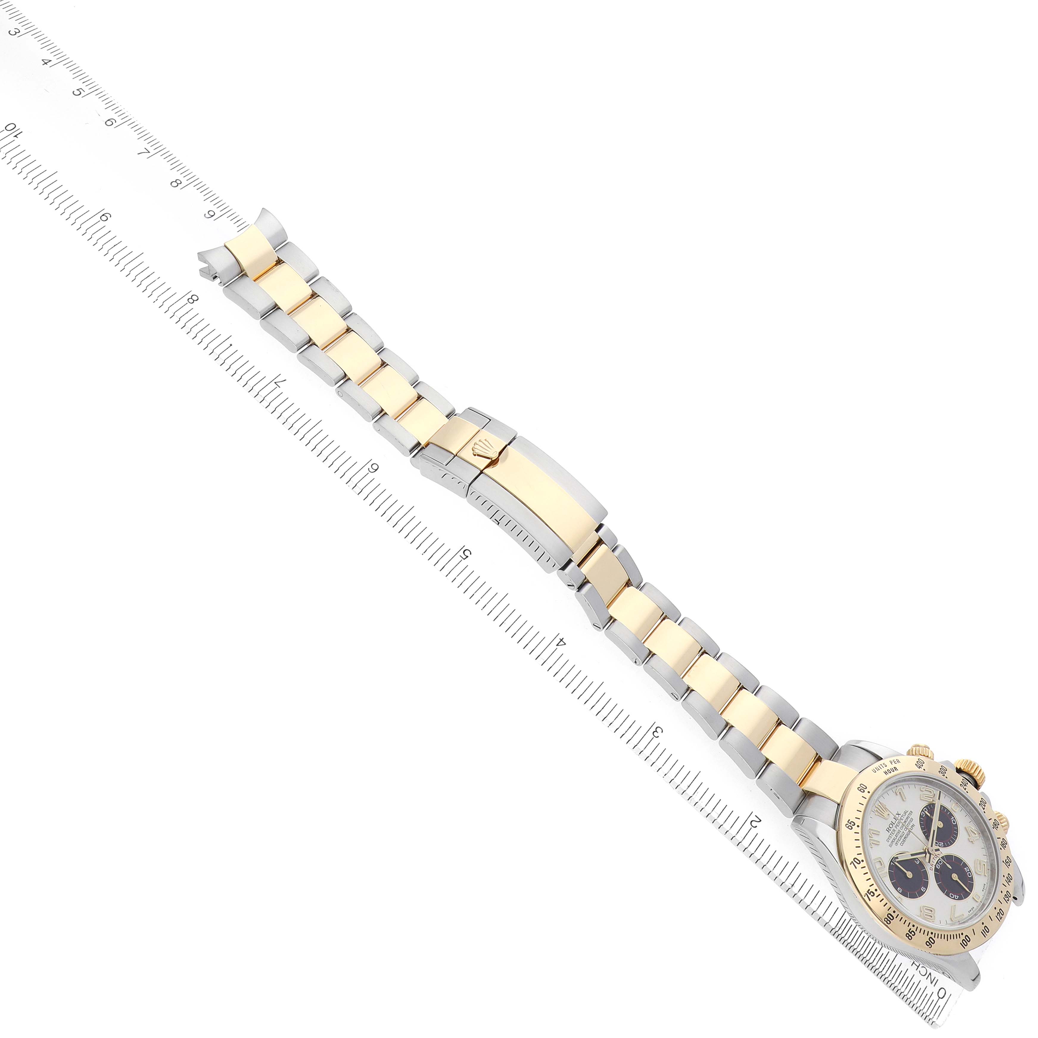 The Rolex Daytona 116523 Men's Steel and Gold (two tone) Silver Dial watch is shown in an overhead angle on top of a ruler, displaying the full bracelet with both gold and silver links and the clasp.