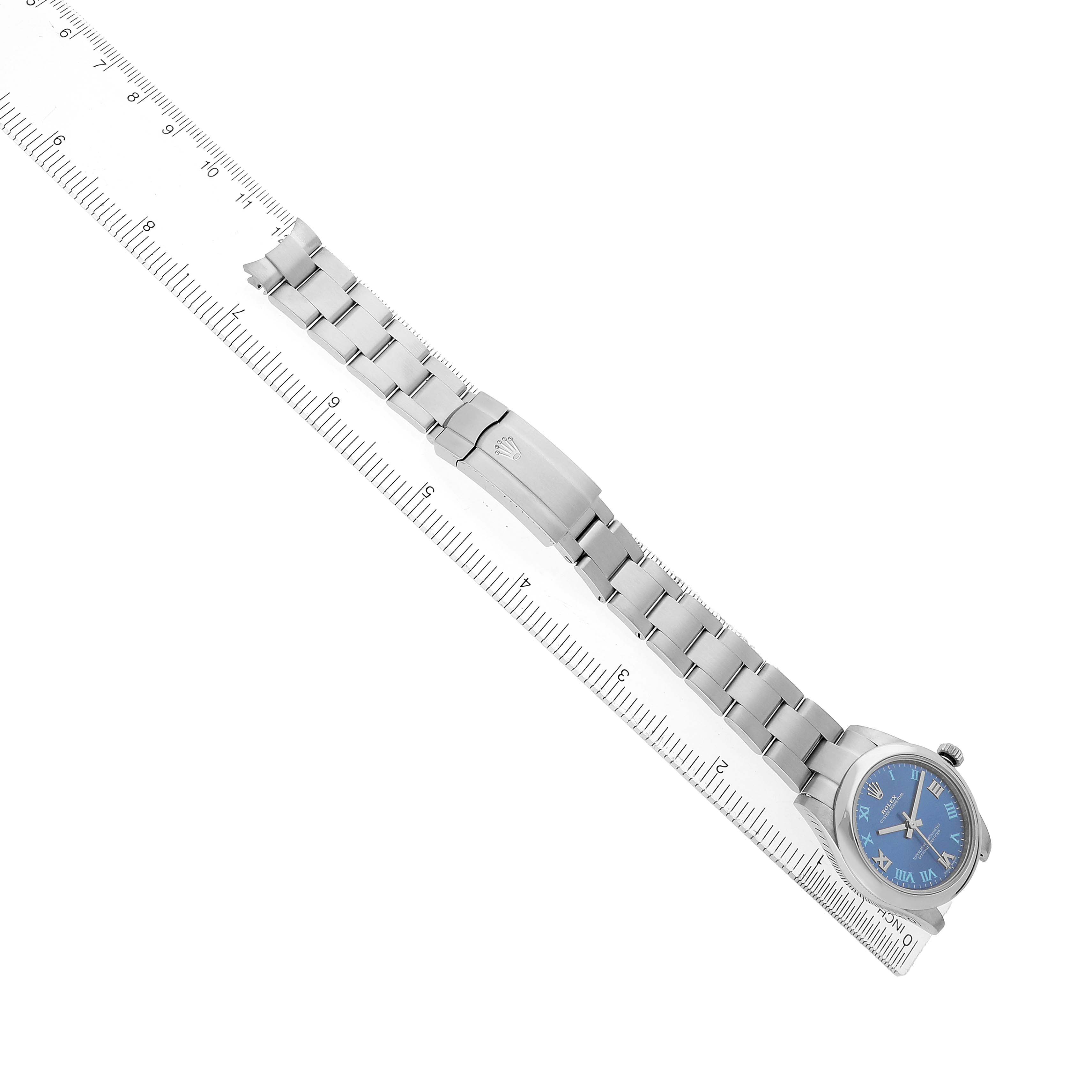 The Rolex Mid-Size 177200 Women's Stainless Steel Blue Dial watch is shown from a top view, highlighting the blue dial and stainless steel bracelet alongside a ruler.
