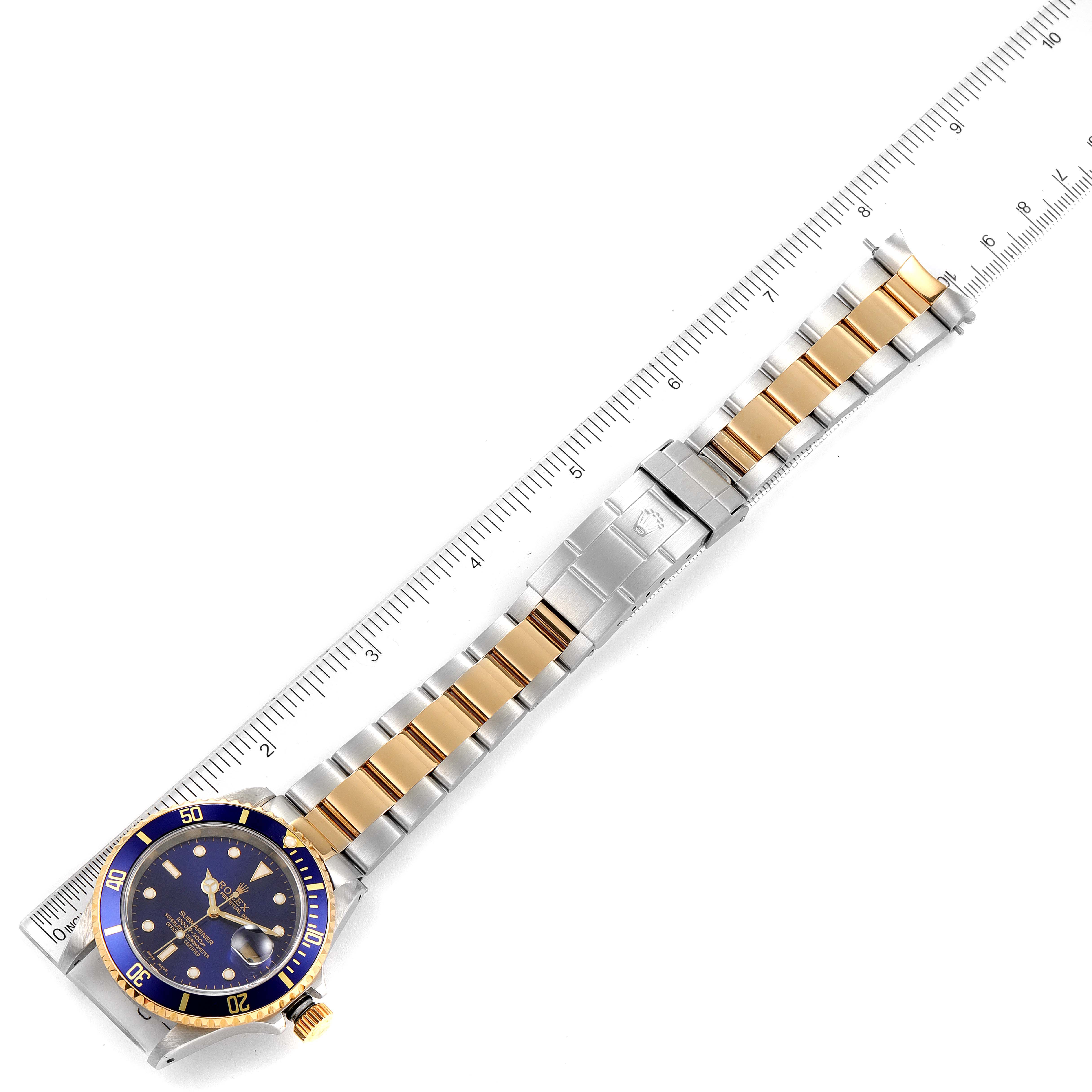 The image shows a top view of a Rolex Submariner 16613 Men
s Steel and Gold (two tone) Blue Dial 16613 Men
s Steel and Gold (two tone) Blue Dial watch with a blue dial and two-tone gold and stainless steel bracelet next to a ruler.