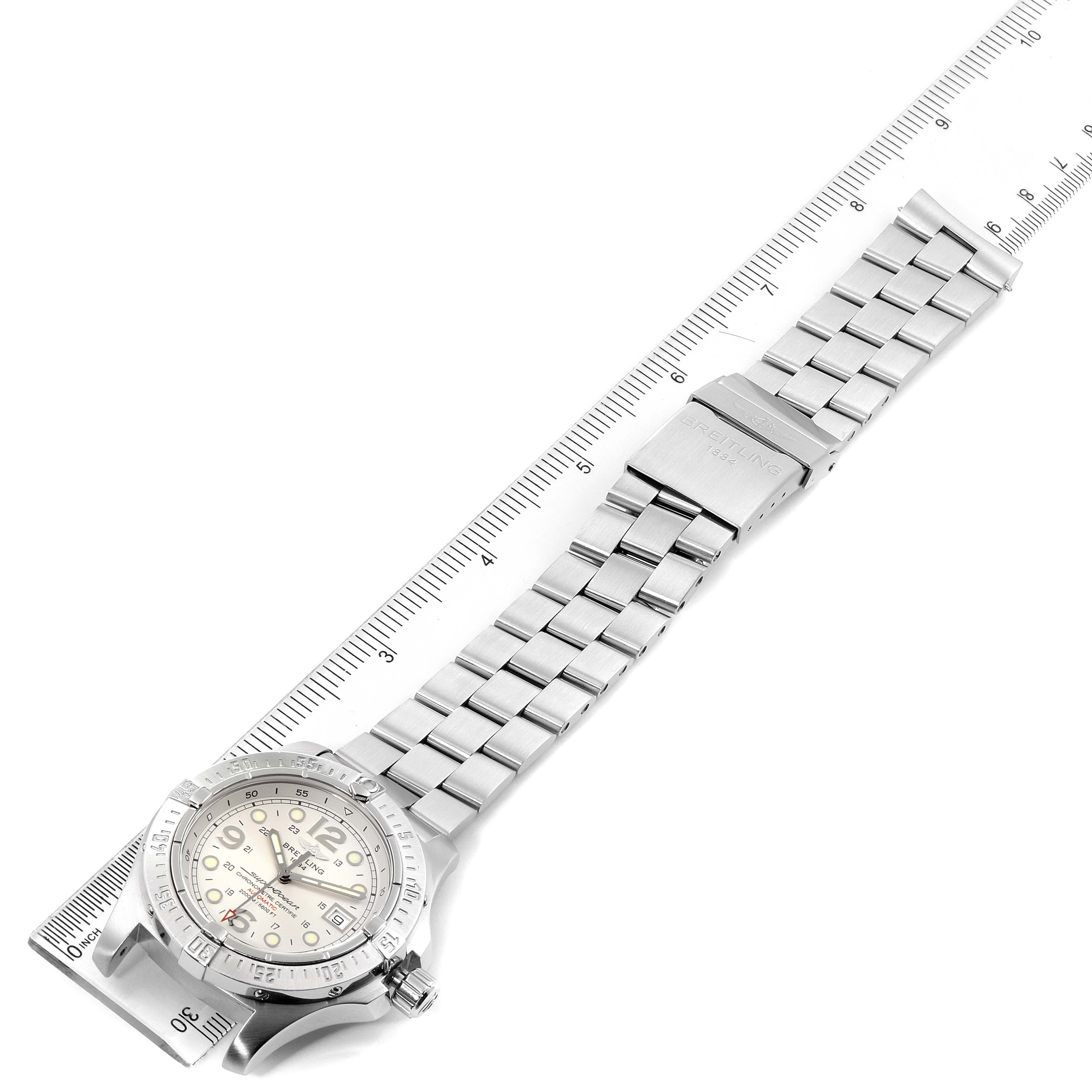 The image shows a top-down view of a Breitling Superocean A17390 Men's Stainless Steel Silver Dial A17390 Men's Stainless Steel Silver Dial watch with its full metal bracelet and clasp, alongside a ruler.