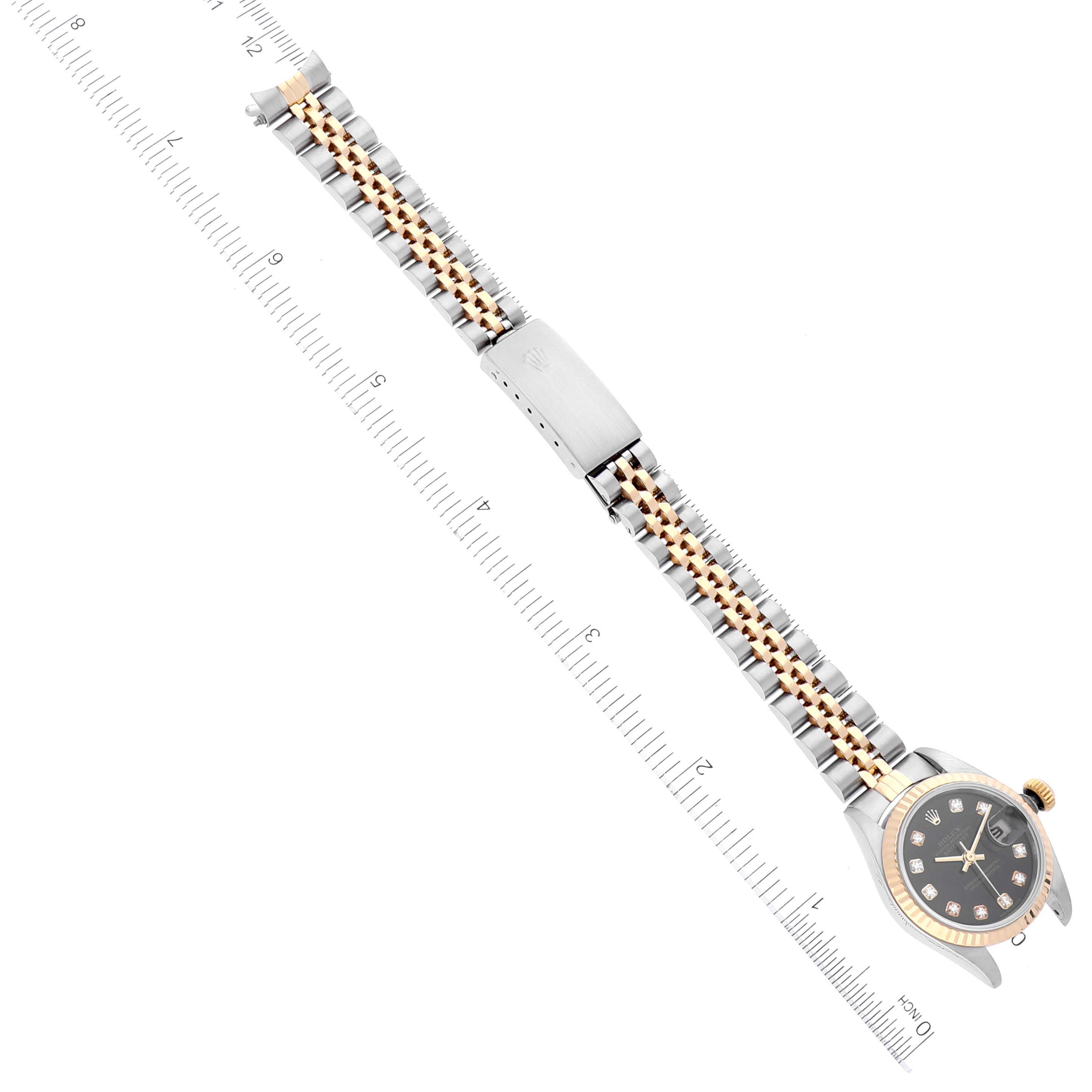 The Rolex Datejust 79173 Women's Steel and Gold (two tone) Black Dial 79173 Women's Steel and Gold (two tone) Black Dial watch is shown from a top view, highlighting its face, bracelet, and clasp, alongside a measurement ruler.