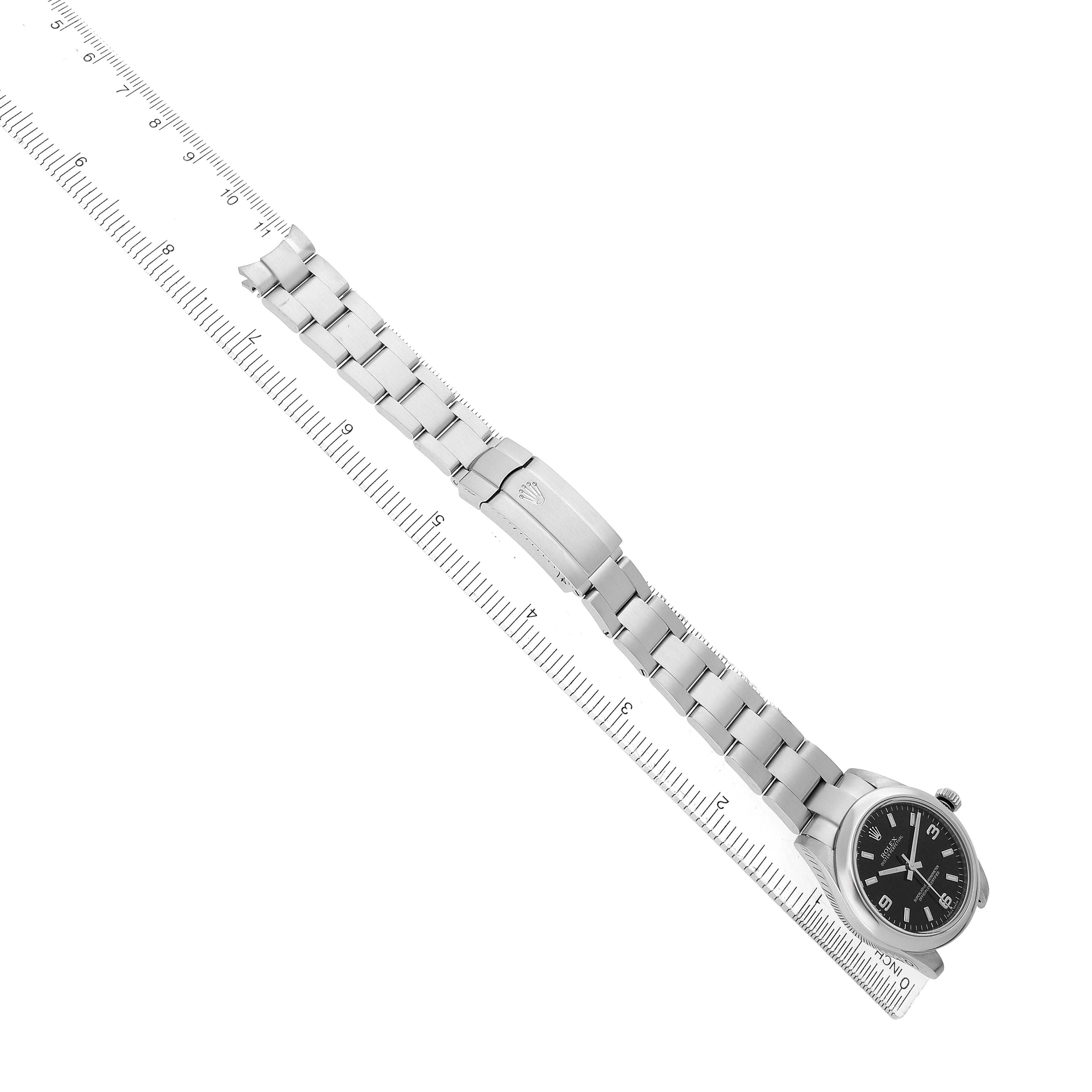 The Rolex Mid-Size 177200 Women's Stainless Steel Black Dial watch is shown from an overhead angle, highlighting the bracelet, clasp, and watch face alongside a ruler.