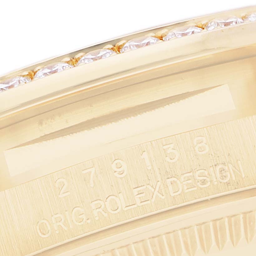 The image shows a close-up of the edge of a Rolex President 279138 Women's Yellow Gold Champagne Dial watch, showcasing the engraved serial numbers and the diamond-set bezel.