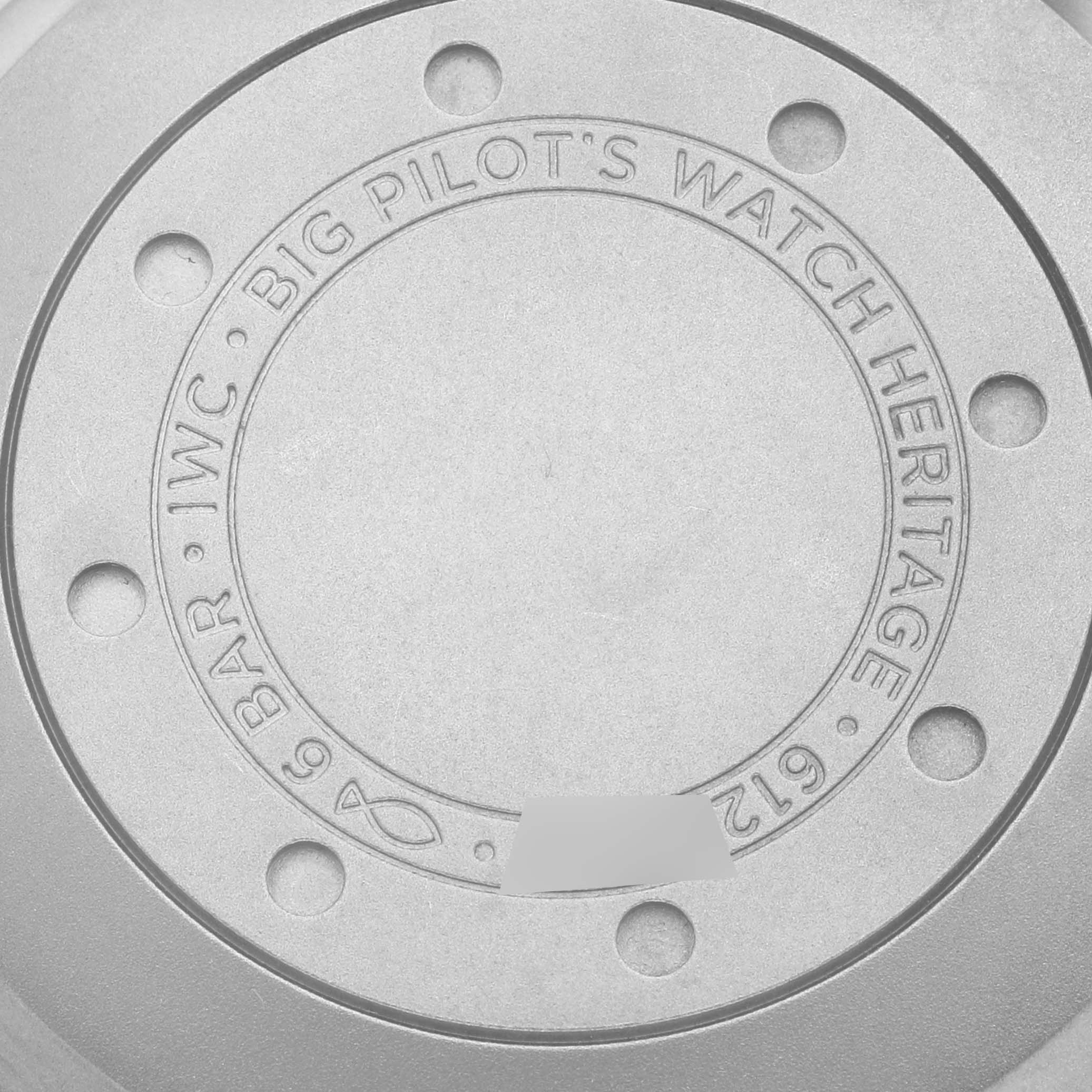 The image shows the back case of the IWC Big Pilot's Watch Heritage, highlighting its engraved text and circular design.