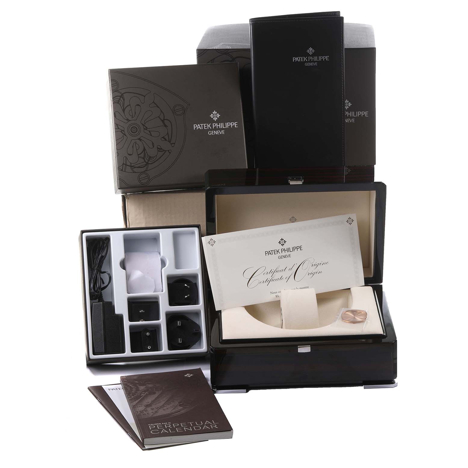 The image shows accessories for the Patek Philippe Complications 5940R - 001 Men's Rose Gold Silver Dial 5940R - 001 Men's Rose Gold Silver Dial model, including a box, certificate, adapters, and manuals.
