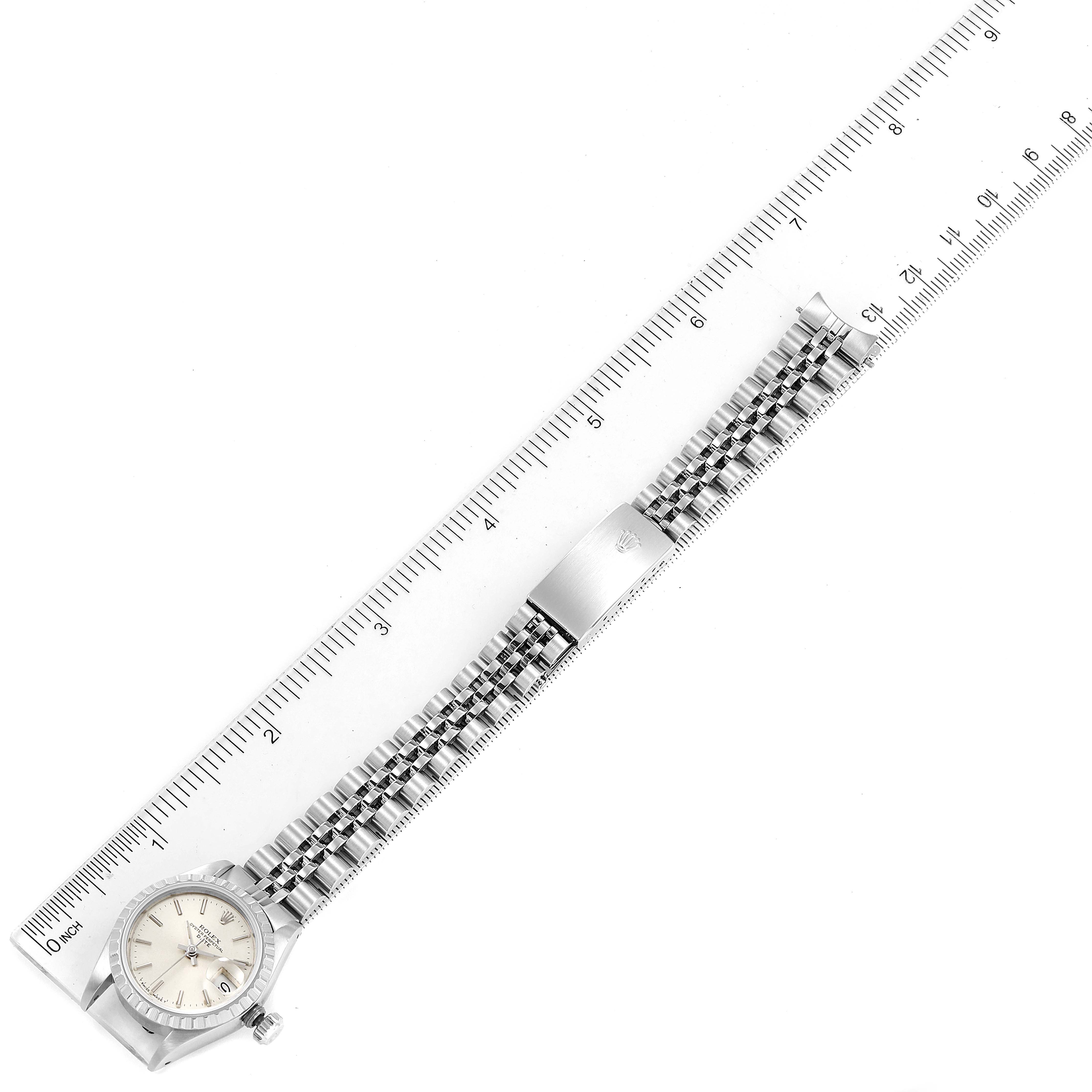 The image shows a Rolex Date 69240 Women
s Stainless Steel Silver Dial 69240 Women
s Stainless Steel Silver Dial watch laid flat alongside a ruler, displaying the face, bracelet, and clasp from a top-down angle.