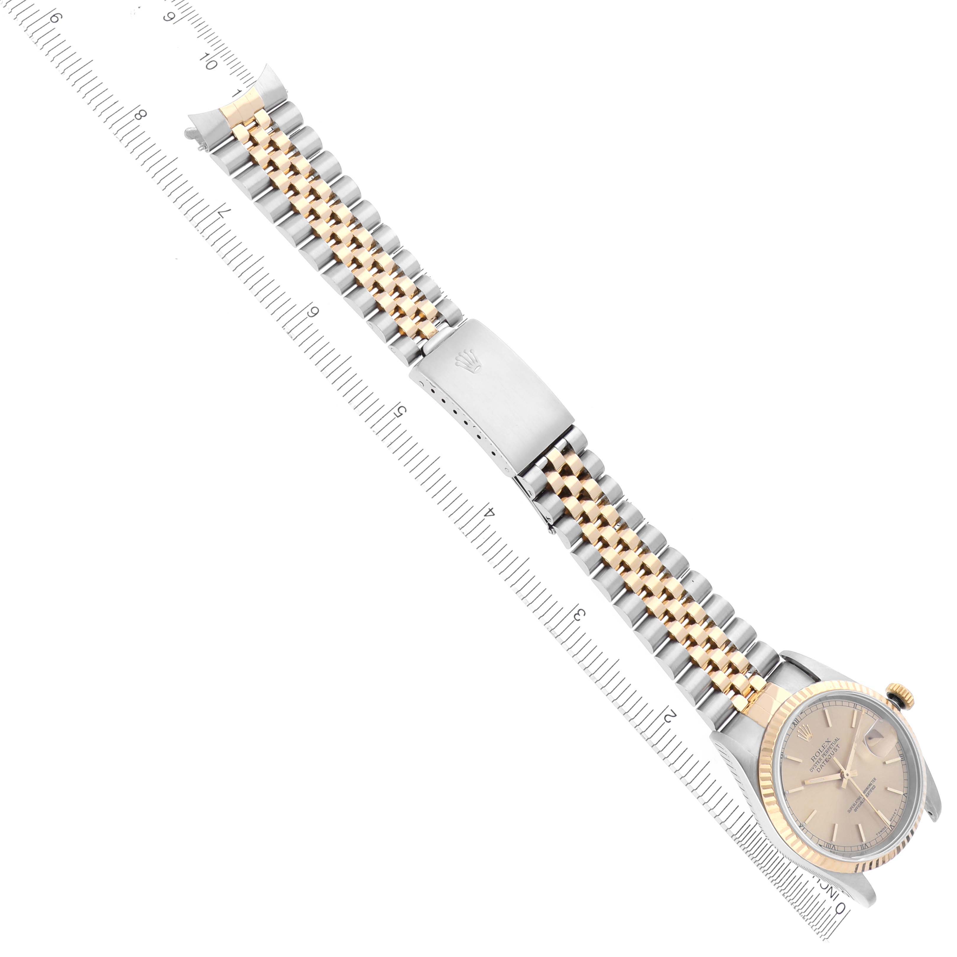The Rolex Datejust 16233 Men's Steel and Gold (two tone) Champagne Dial 16233 Men's Steel and Gold (two tone) Champagne Dial watch is shown from a top view, highlighting its face and full two-tone bracelet with clasp alongside a ruler.