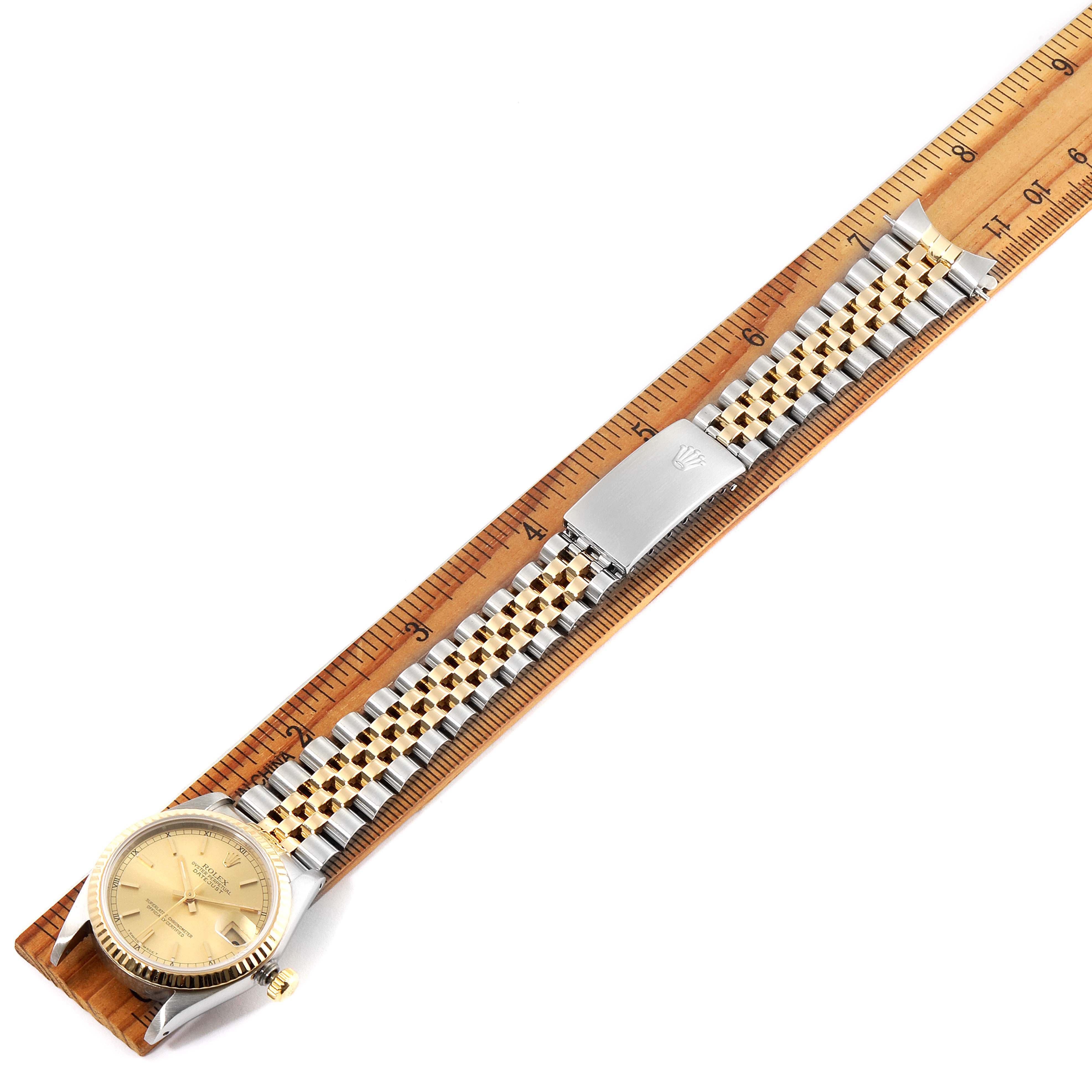 This is a top-down view of a Mid-Size Rolex watch, showing the face, band, and clasp placed against a ruler.