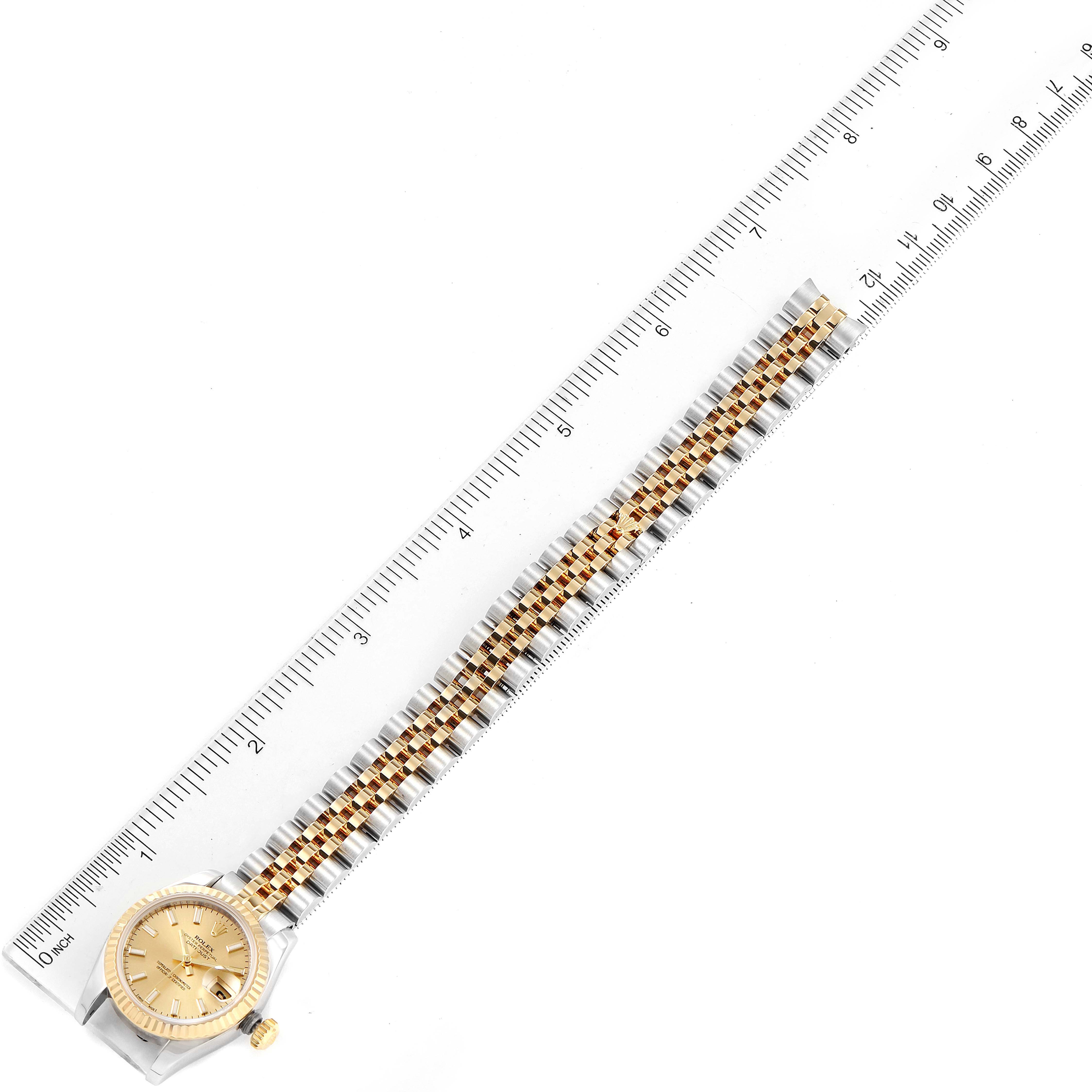 The image shows a Rolex Datejust 179173 Women's Steel and Gold (two tone) Champagne Dial 179173 Women's Steel and Gold (two tone) Champagne Dial watch laid flat next to a ruler, highlighting its bracelet and face at a top-down angle.