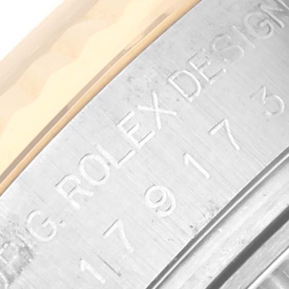 The image shows a close-up of the edge of a Rolex Datejust 179173 Women's Steel and Gold (two tone) White Dial 179173 Women's Steel and Gold (two tone) White Dial, focusing on the engraved text on the bezel and case.