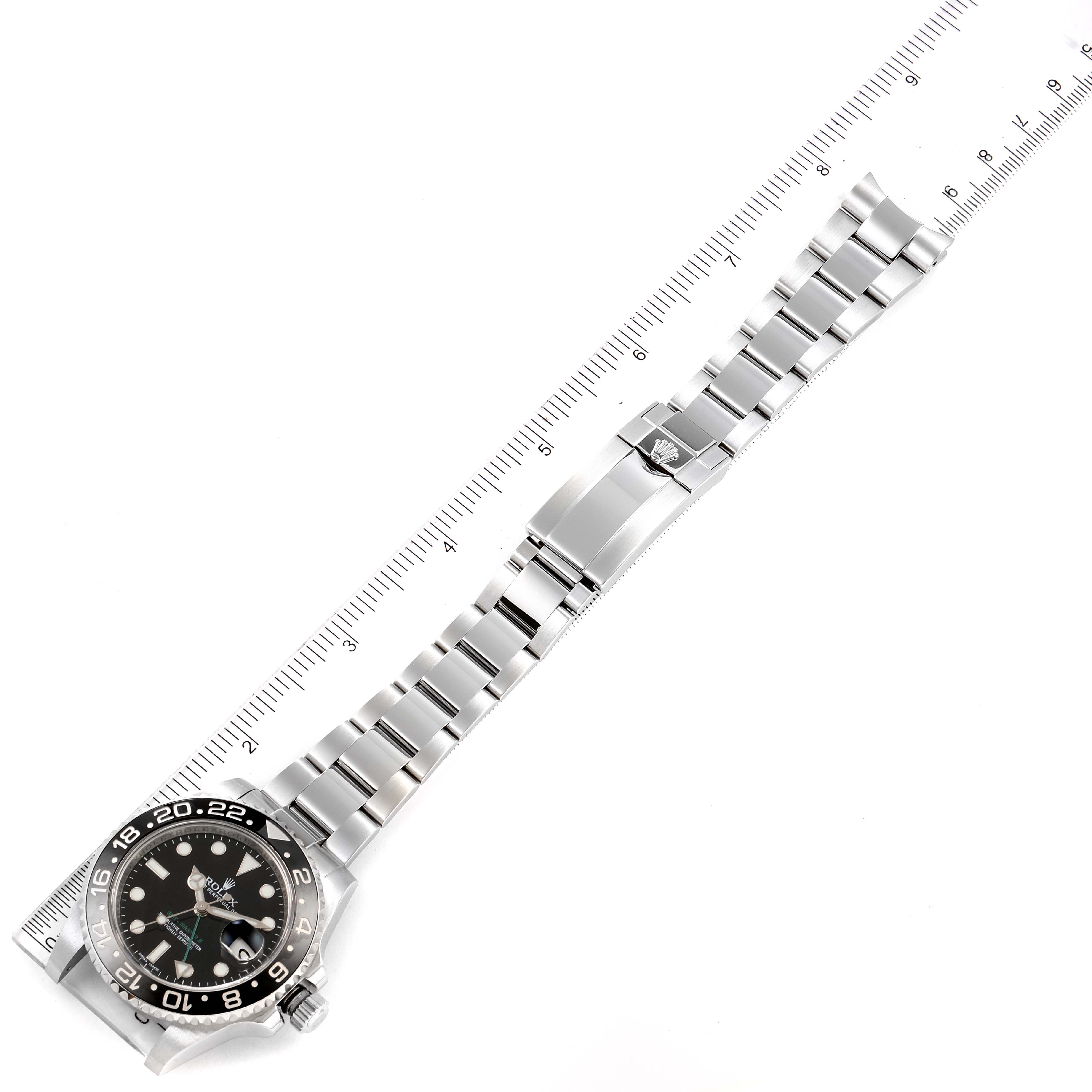 The image shows a top-down view of a Rolex GMT-Master 116710 Men
s Stainless Steel Black Dial 116710 Men
s Stainless Steel Black Dial watch and its bracelet fully extended alongside a ruler.