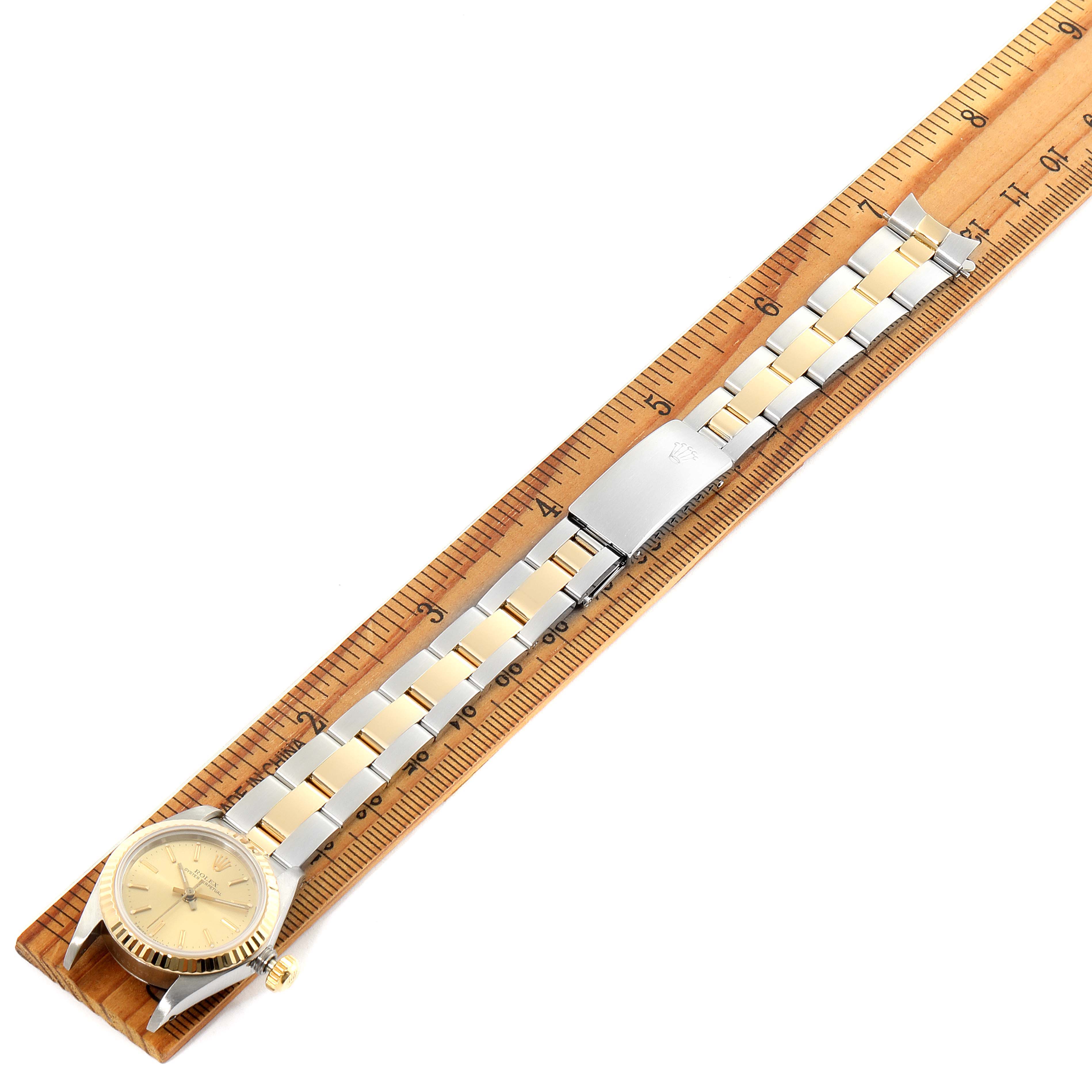 The Rolex Oyster Perpetual 67193 Women
s Steel and Gold (two tone) Champagne Dial 67193 Women
s Steel and Gold (two tone) Champagne Dial watch is shown laying flat on a wooden ruler, displaying its full band and watch face.