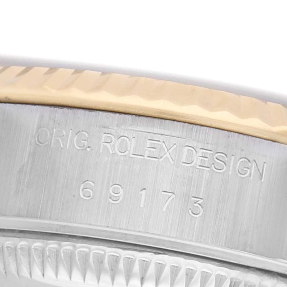 The image shows a close-up of a Rolex Datejust 69173 Women's Steel and Gold (two tone) Blue Dial watch case side with engravings, focusing on the model number and design details.
