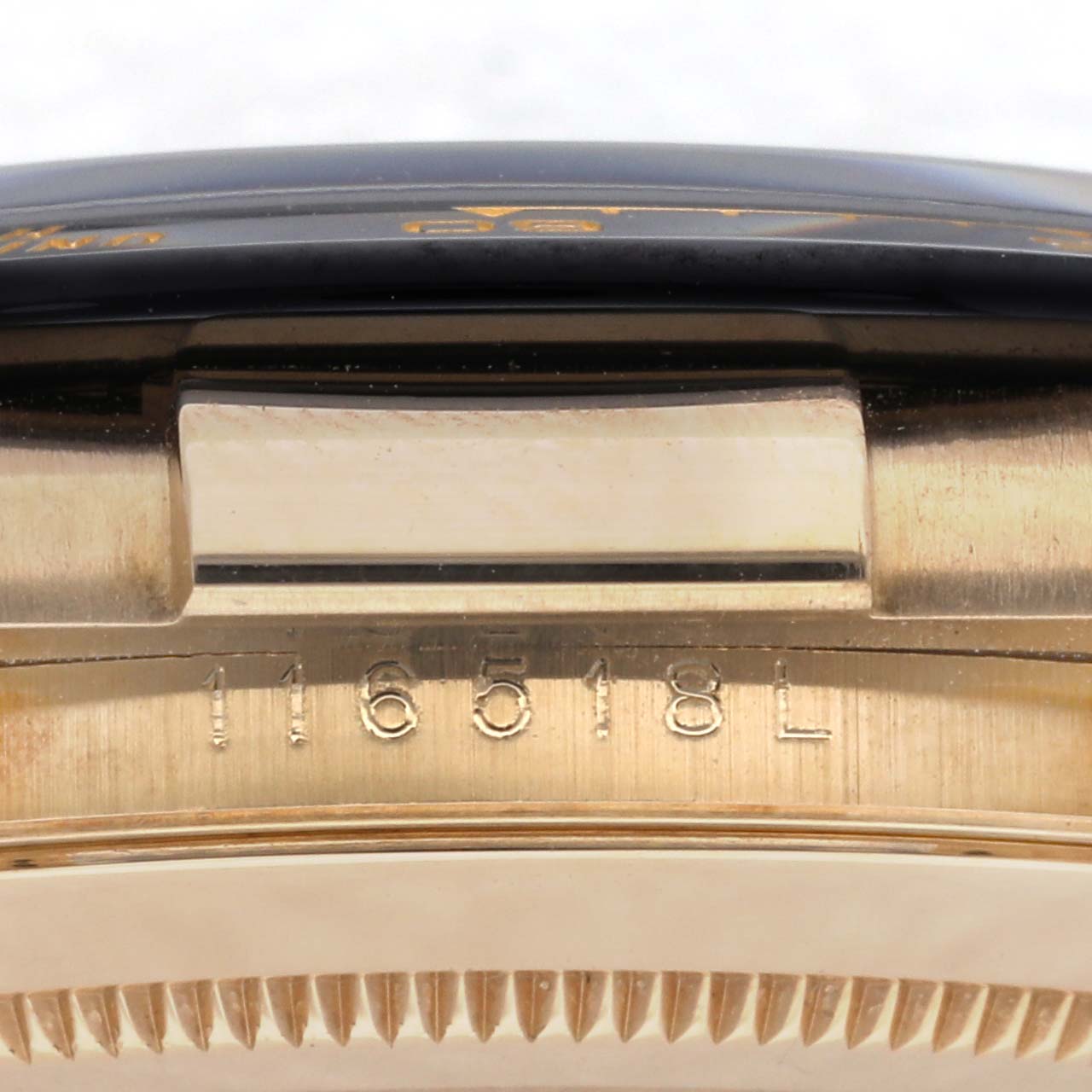 The image shows a side view of the Rolex Daytona 116518 Men
s Yellow Gold Black Dial 116518 Men
s Yellow Gold Black Dial, focusing on the bezel edge and engraved serial number.