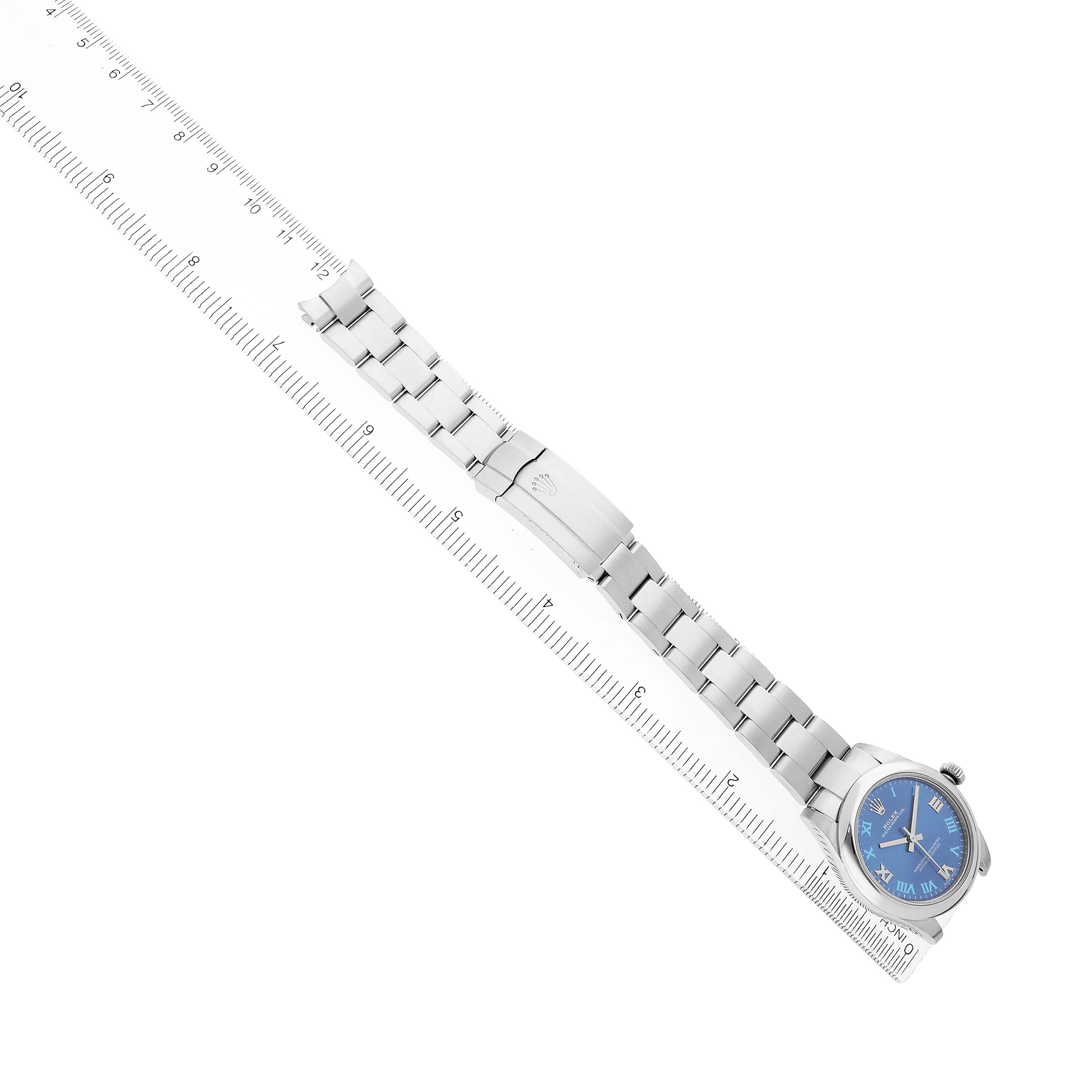 The Rolex Mid-Size 177200 Women's Stainless Steel Blue Dial watch is shown from a top-down angle, displaying the face, bracelet, and clasp alongside a ruler.