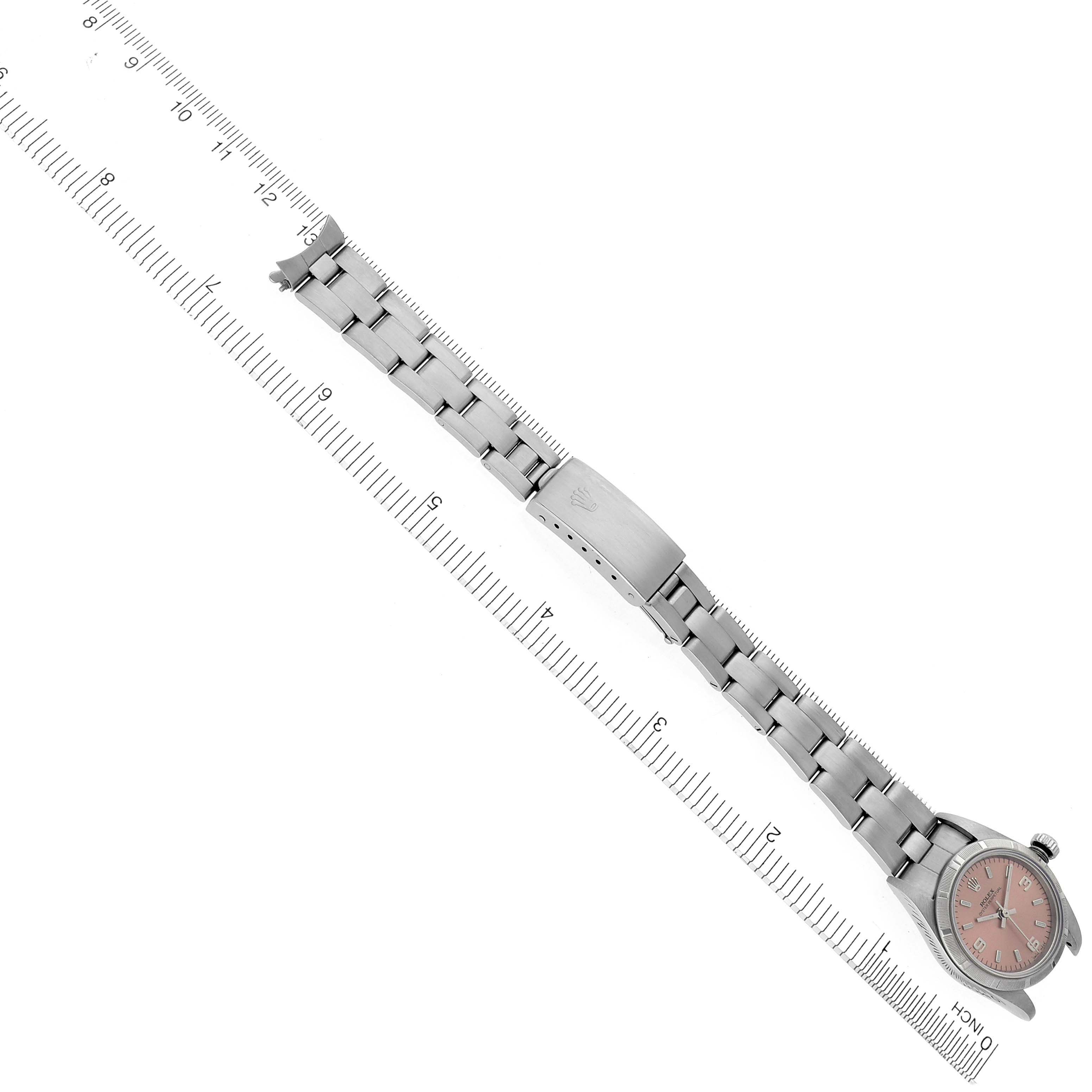 The Rolex Oyster Perpetual 76030 Women's Stainless Steel Pink Dial 76030 Women's Stainless Steel Pink Dial watch is shown from an angled top view, displaying the bracelet and clasp alongside a ruler.