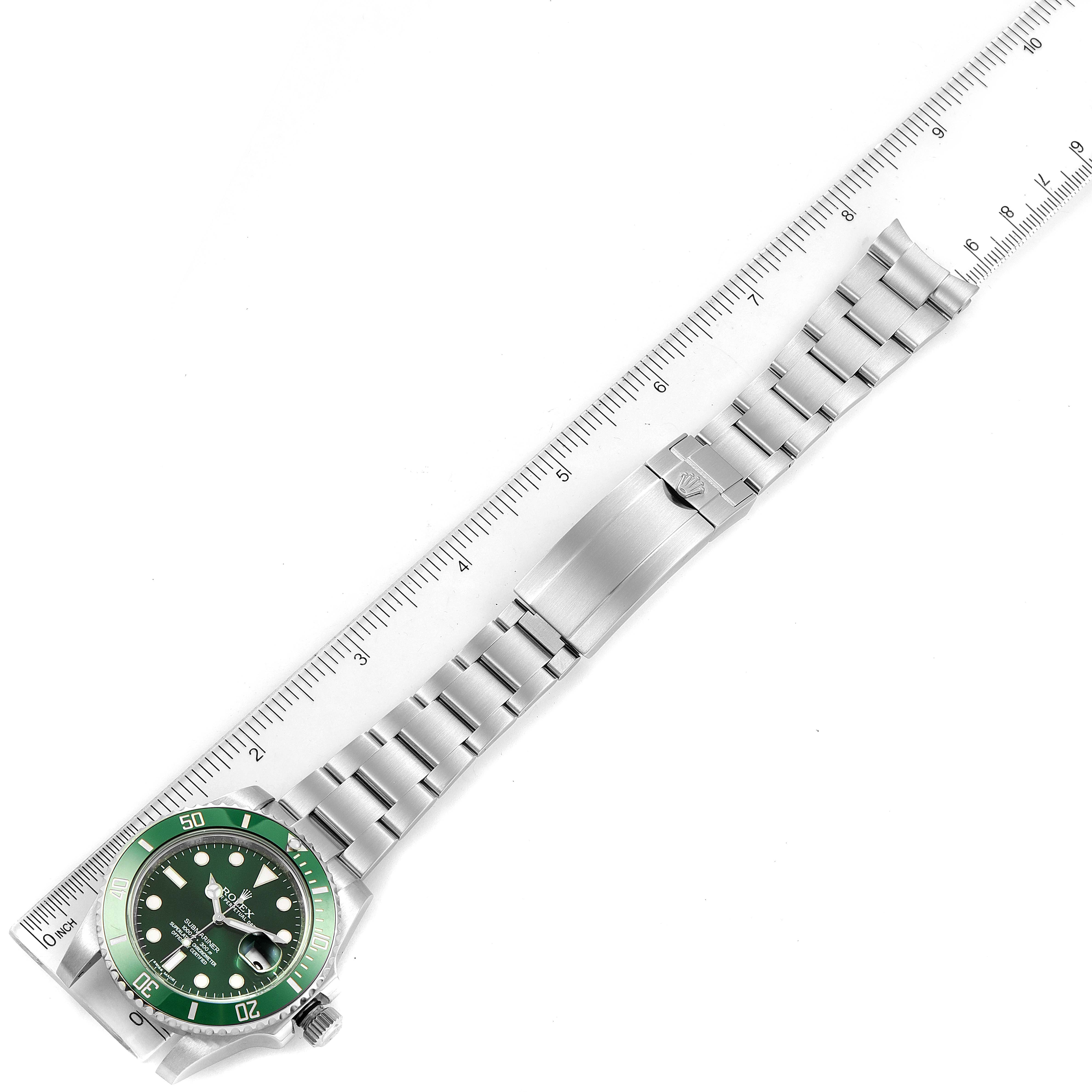 The image shows the full view of a Rolex Submariner 116610LV Men
s Stainless Steel Green Dial 116610LV Men
s Stainless Steel Green Dial watch laid flat with a metal bracelet alongside a ruler.