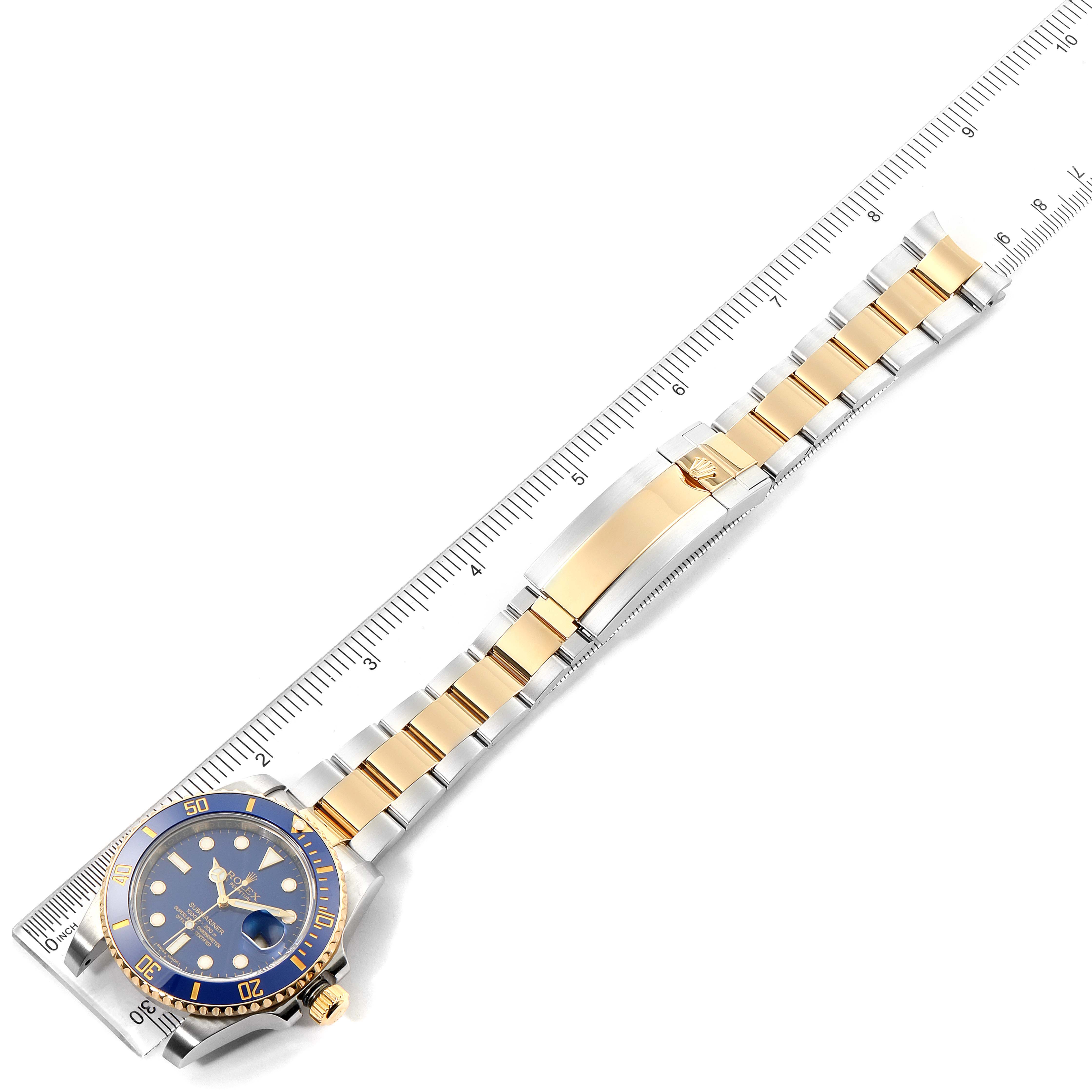 The image shows the front view of a Rolex Submariner 116613 Men's Steel and Gold (two tone) Blue Dial 116613 Men's Steel and Gold (two tone) Blue Dial watch with a gold and silver bracelet, alongside a ruler for scale.