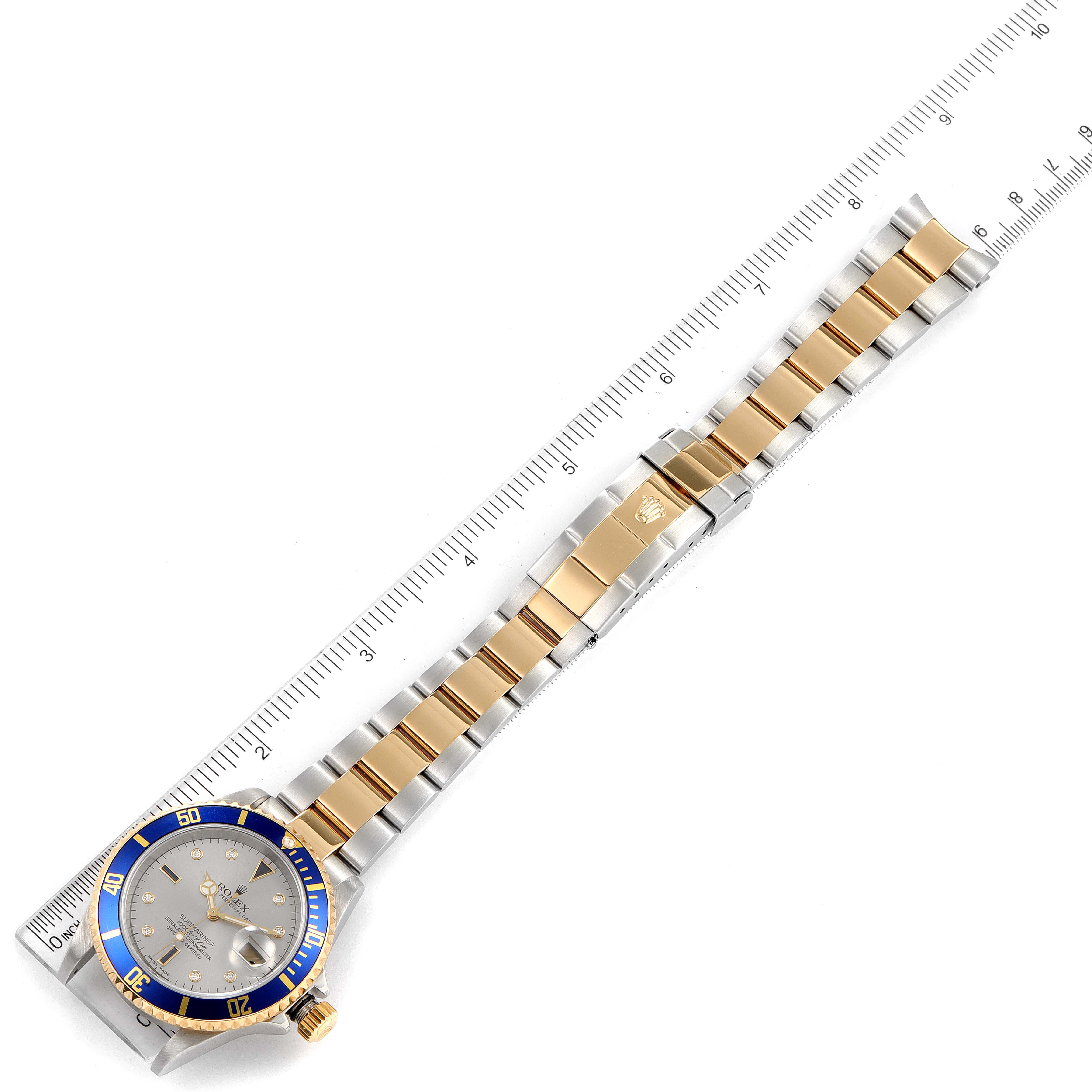 The image shows a Rolex Submariner 16613 Men's Steel and Gold (two tone) Grey Dial 16613 Men's Steel and Gold (two tone) Grey Dial watch laid flat beside a ruler, featuring the strap and watch face.