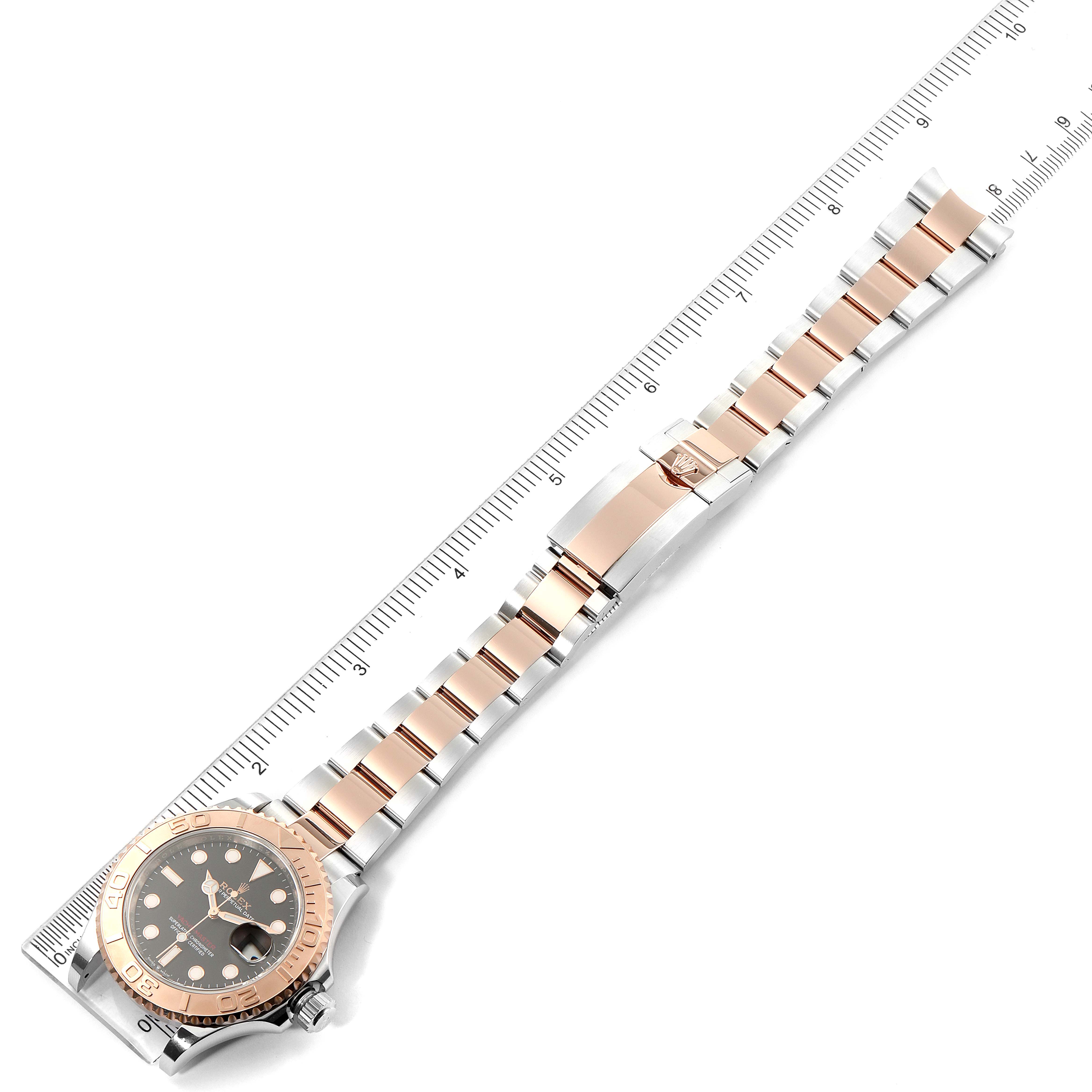 This image shows the Rolex Yacht-Master 126621 Men's Rose Gold Black Dial 126621 Men's Rose Gold Black Dial watch lying flat with a full view of the watch face and bracelet alongside a ruler for scale.