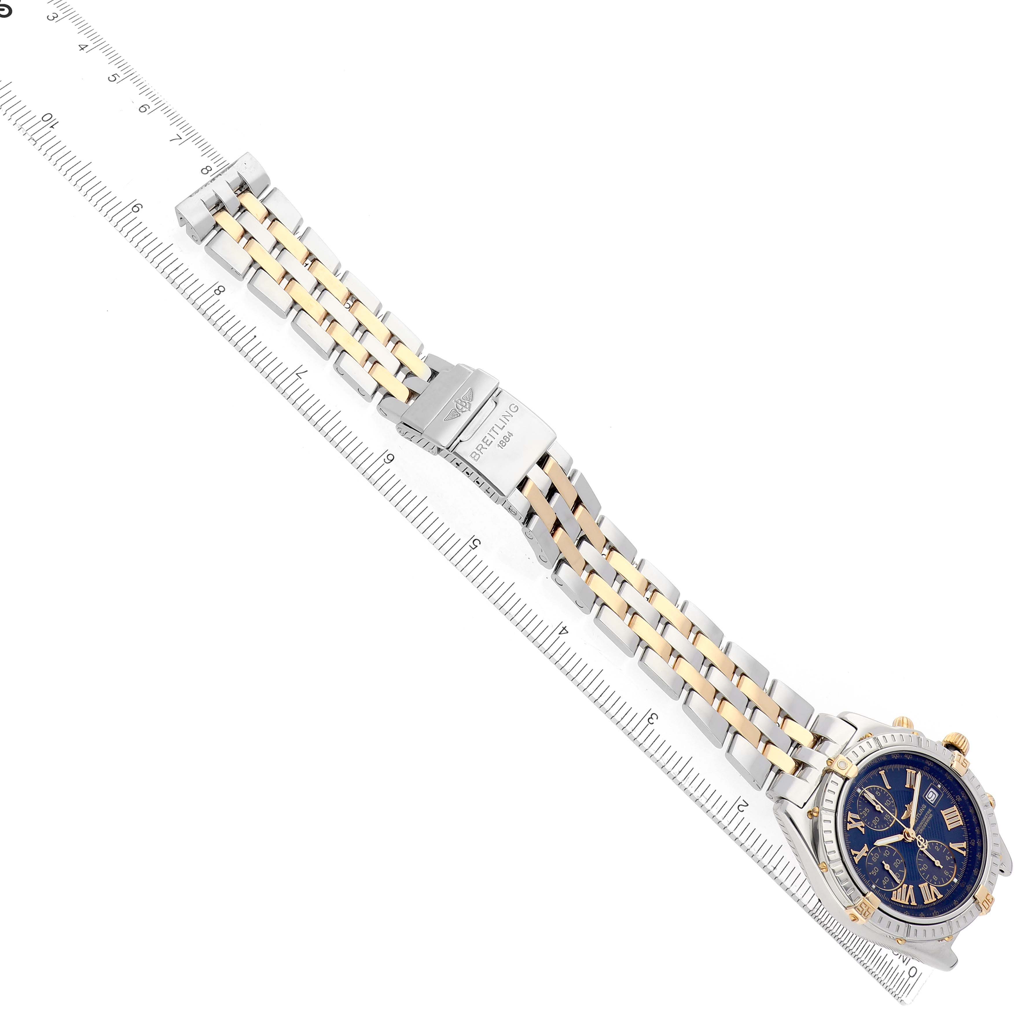 The Breitling Windrider B13355 Men's Steel and Gold (two tone) Blue Dial watch is shown from a top-down angle, highlighting its face and two-tone bracelet against a ruler.