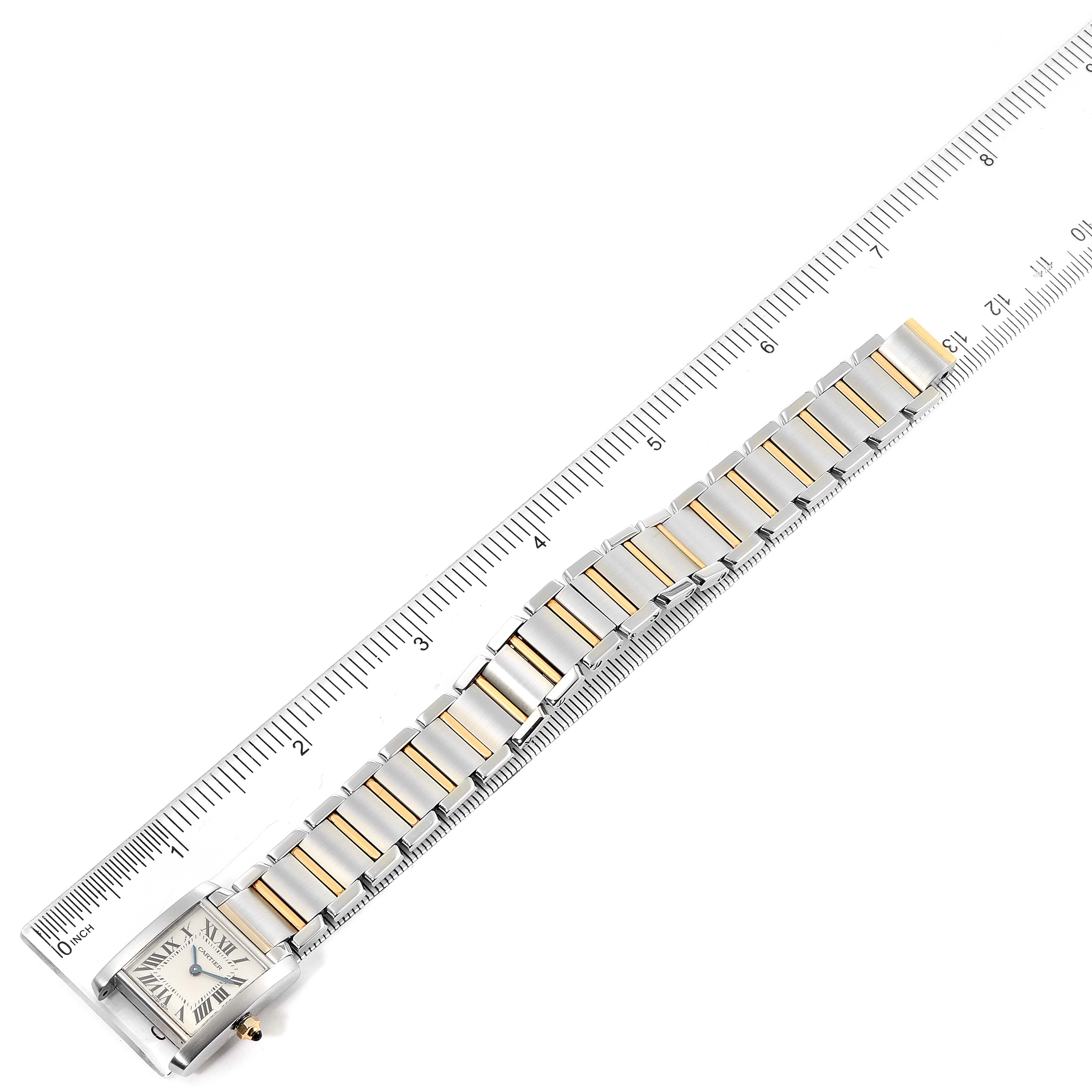 The Cartier Tank Française watch is shown from a top-down angle, featuring the face and the metal bracelet next to a ruler for scale.