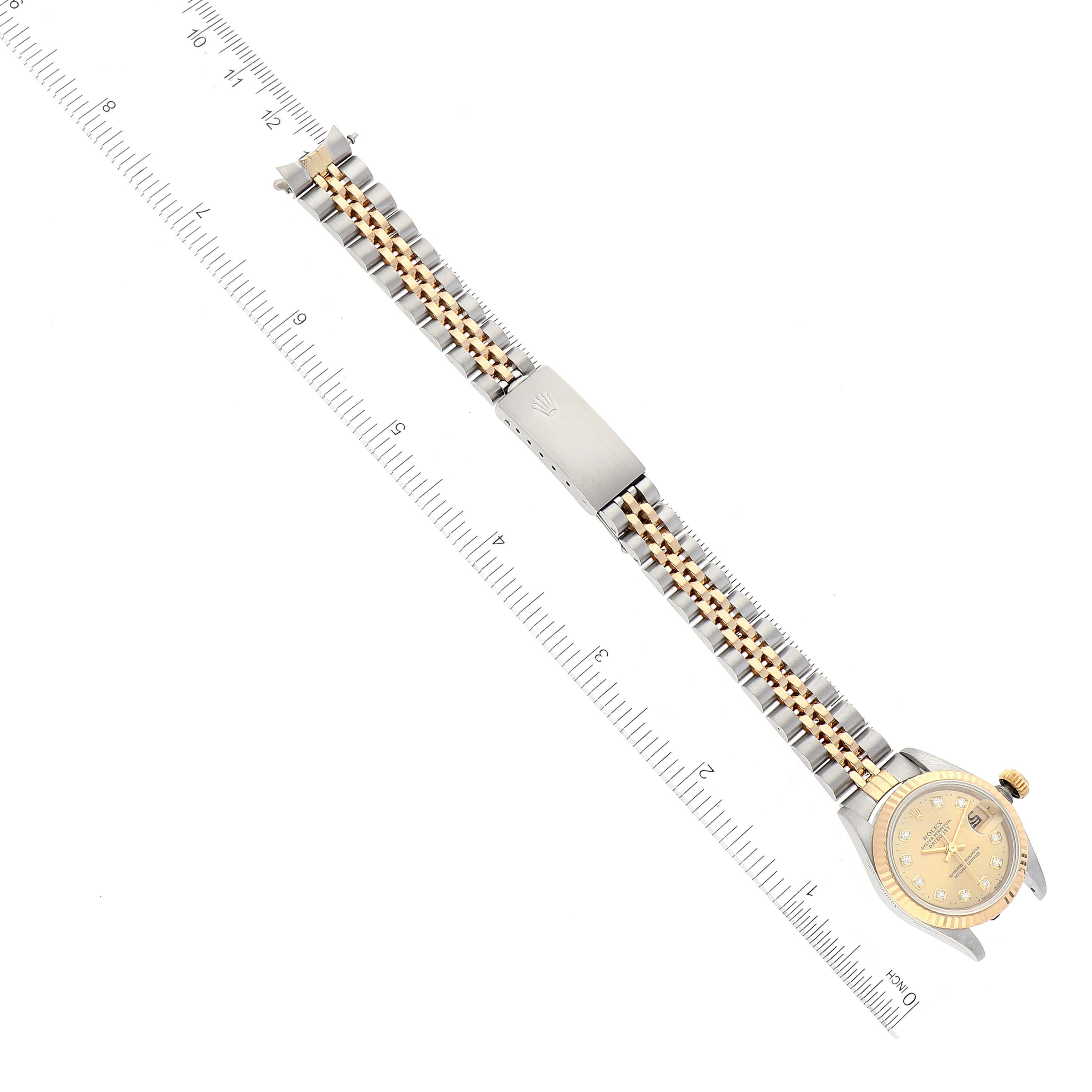 The Rolex Datejust 69173 Women's Steel and Gold (two tone) Champagne Dial 69173 Women's Steel and Gold (two tone) Champagne Dial watch is shown from a top-down angle, displaying its face, bezel, bracelet, and clasp alongside a ruler for scale.