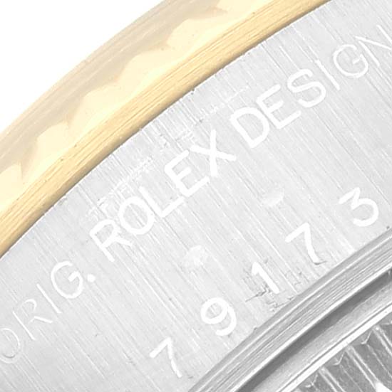 This image shows a close-up of the edge of a Rolex Datejust 79173 Women's Steel and Gold (two tone) White Dial 79173 Women's Steel and Gold (two tone) White Dial watch case featuring part of the bezel and engraved text.