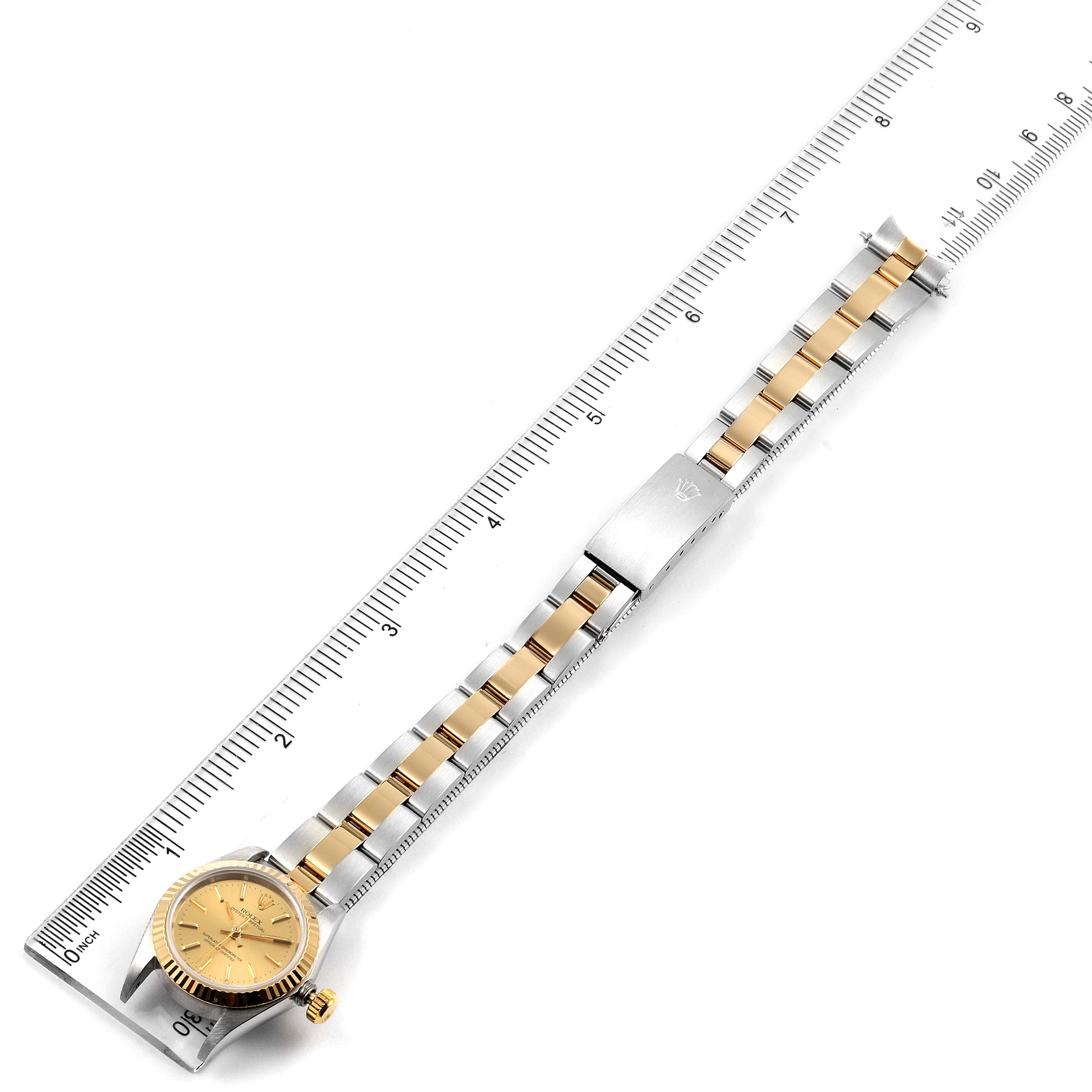 The image shows a top-down view of a gold and silver Rolex Oyster Perpetual 67193 Women
s Steel and Gold (two tone) Champagne Dial 67193 Women
s Steel and Gold (two tone) Champagne Dial watch alongside a ruler.