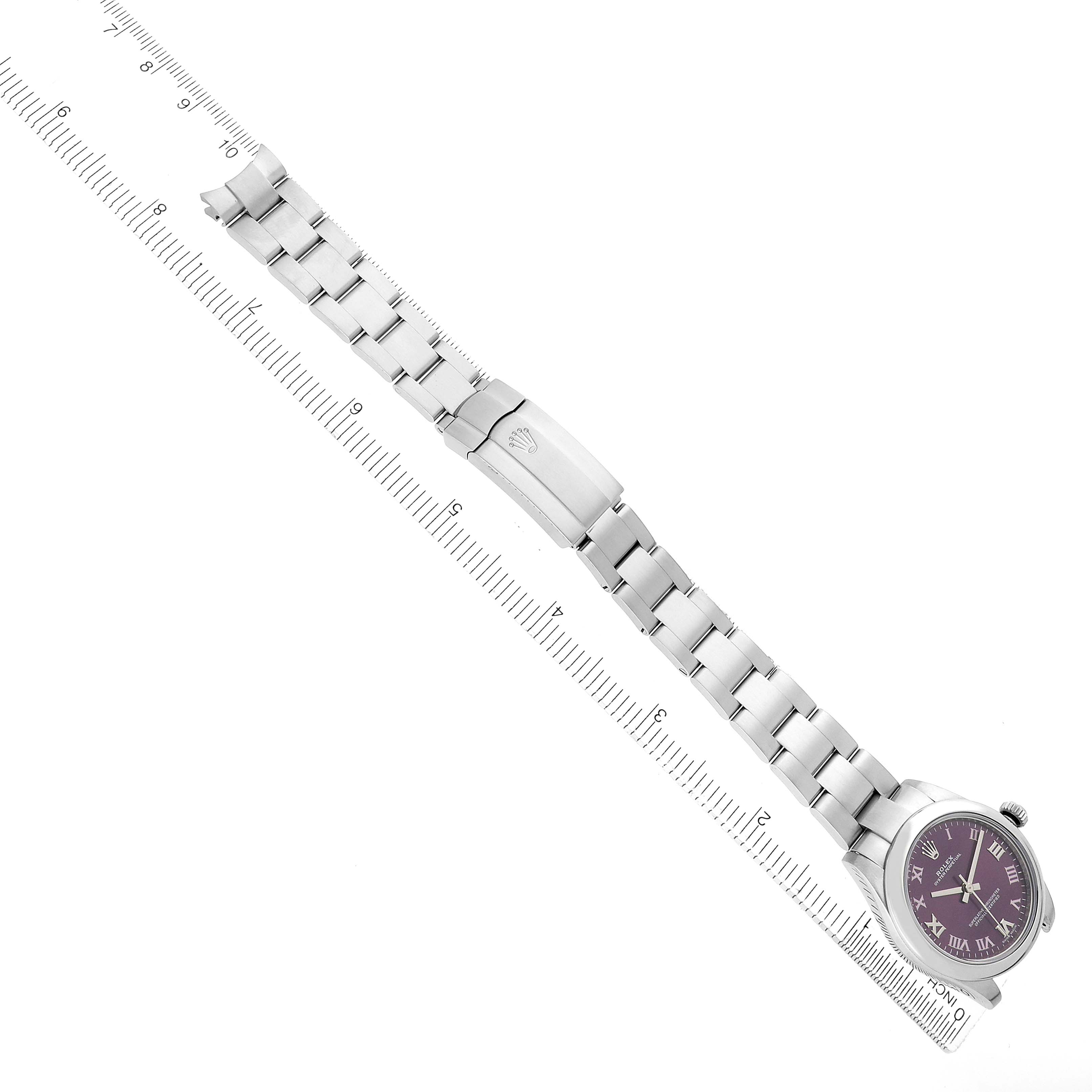 The Rolex Mid-Size 177200 Women's Stainless Steel Purple Dial watch is shown from a top-down angle, highlighting the bracelet, clasp, and face, alongside a ruler for scale.