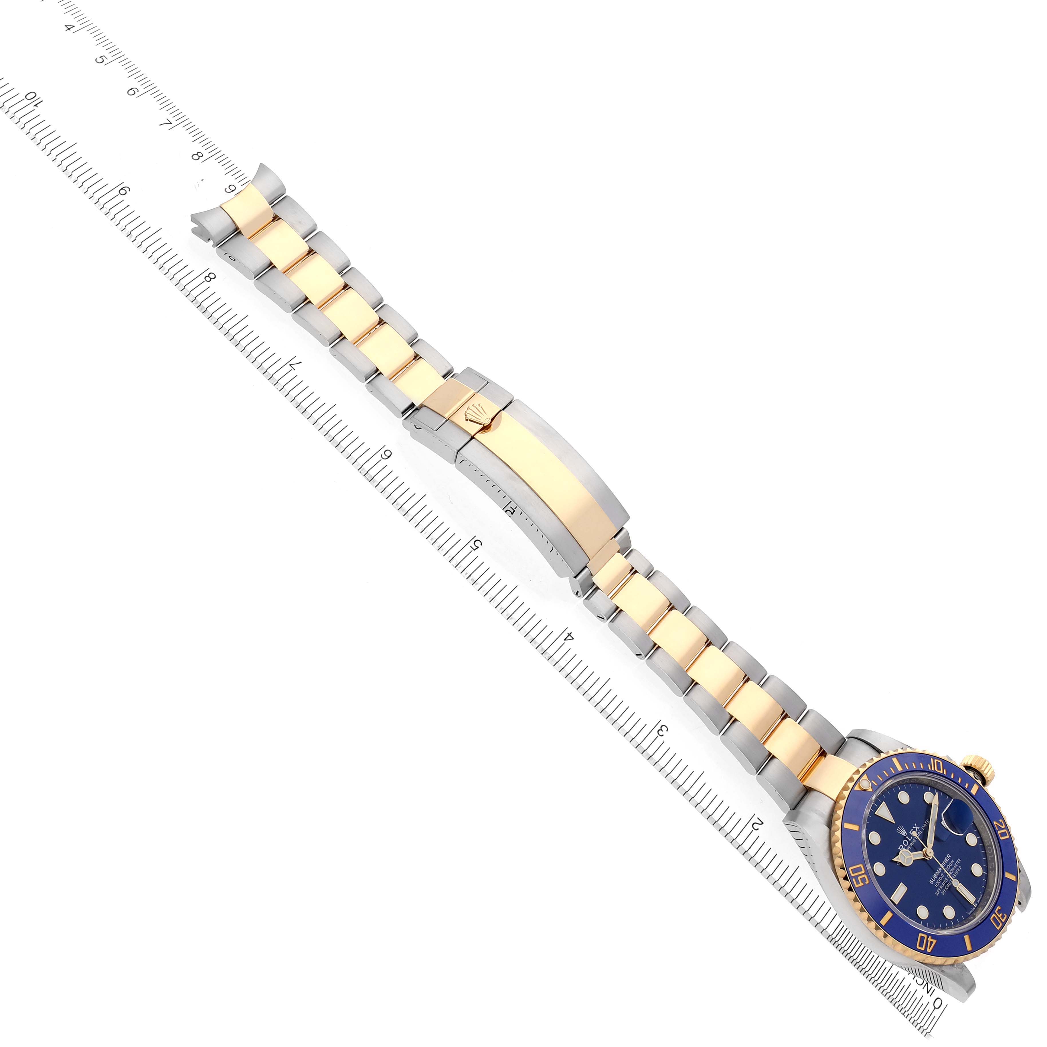 The image shows a Rolex Submariner 126613LB Men's Steel and Gold (two tone) Blue Dial 126613LB Men's Steel and Gold (two tone) Blue Dial watch fully extended, highlighting the bracelet and clasp, placed diagonally on a ruler.
