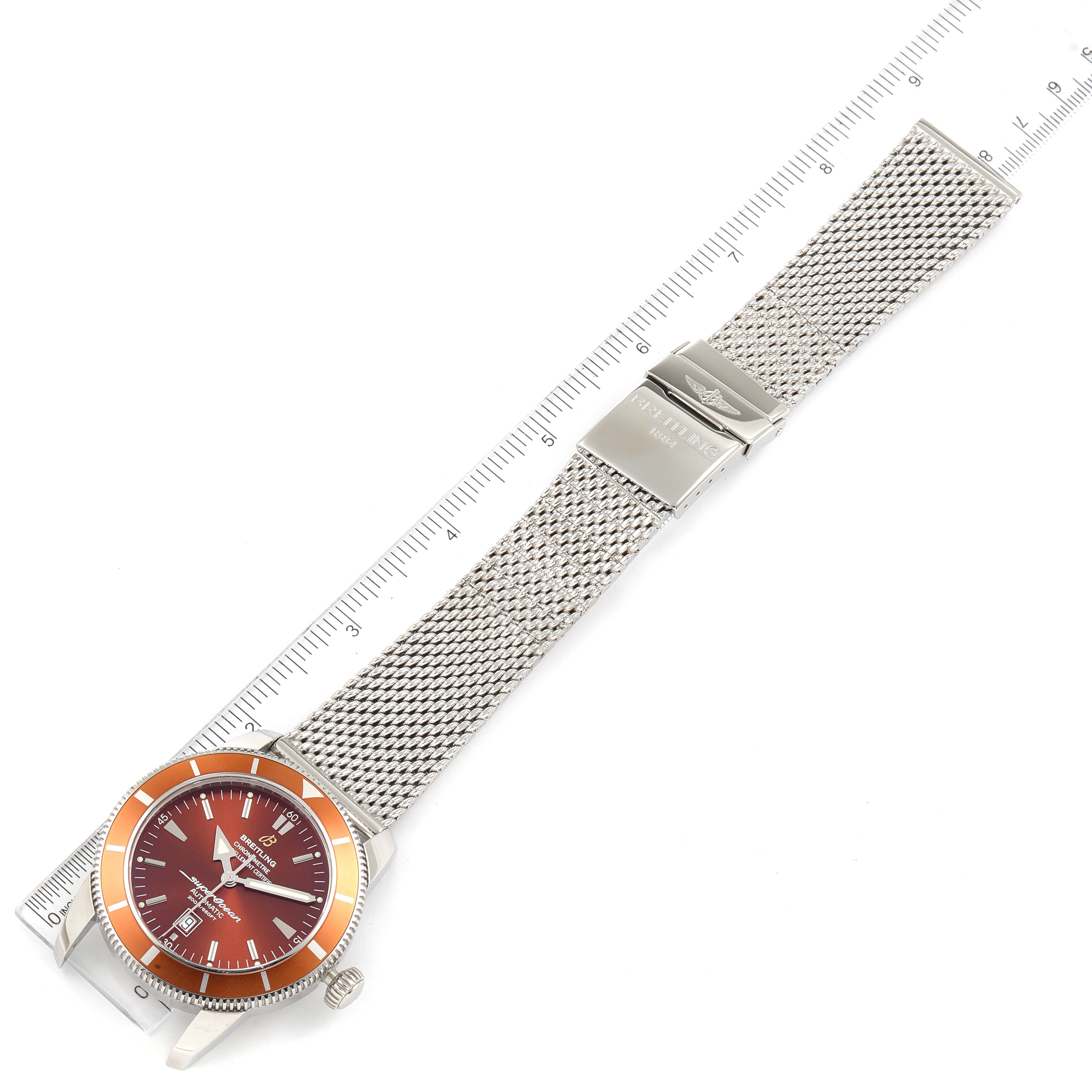 The image shows a top-down view of a Breitling Superocean A17320 Men's Stainless Steel Brown Dial A17320 Men's Stainless Steel Brown Dial watch, displaying the dial, bezel, and mesh strap alongside a ruler.