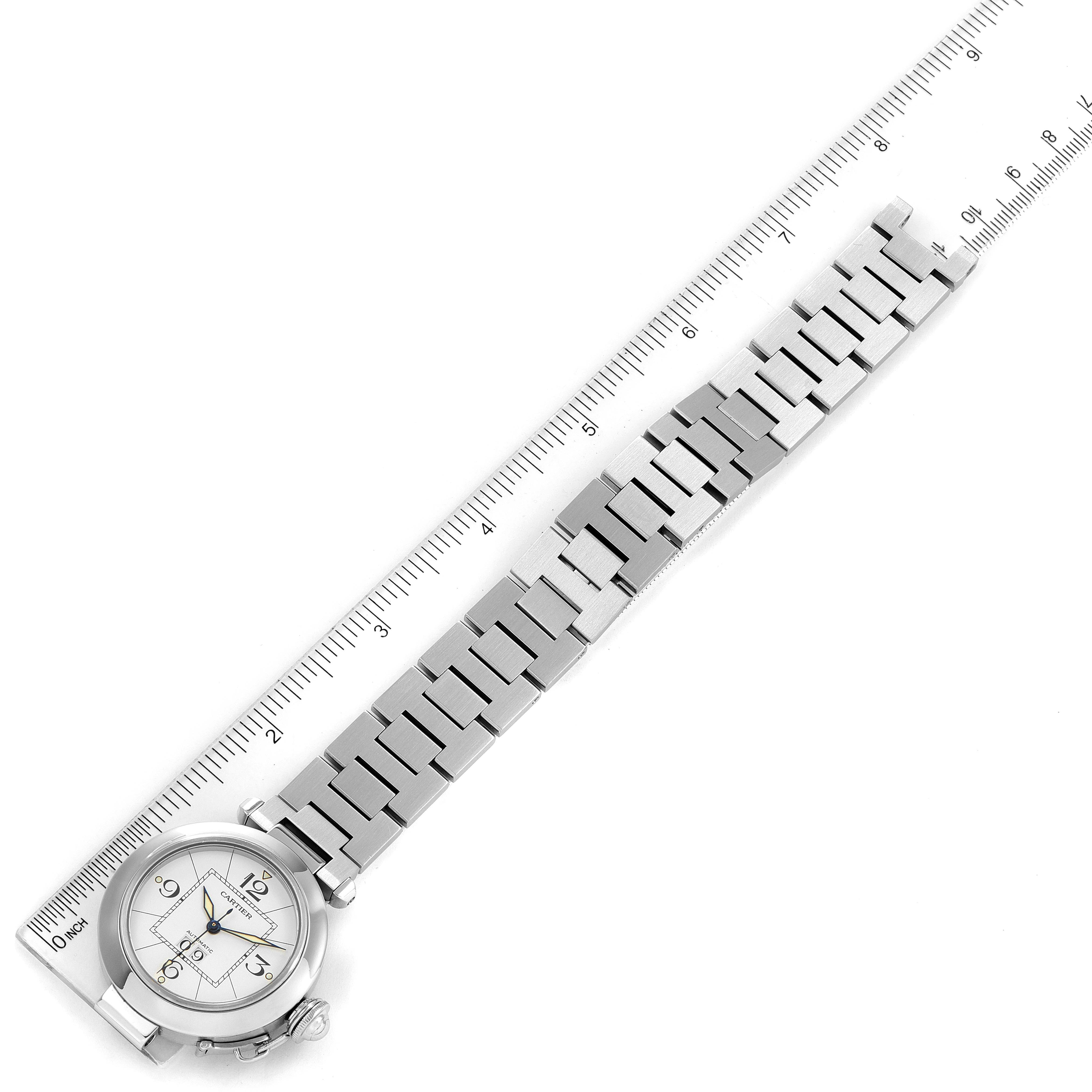 The image shows a top view of the entire Cartier Pasha W31055M7 Women's Stainless Steel White Dial W31055M7 Women's Stainless Steel White Dial watch, including its face and metal bracelet, alongside a ruler for scale.