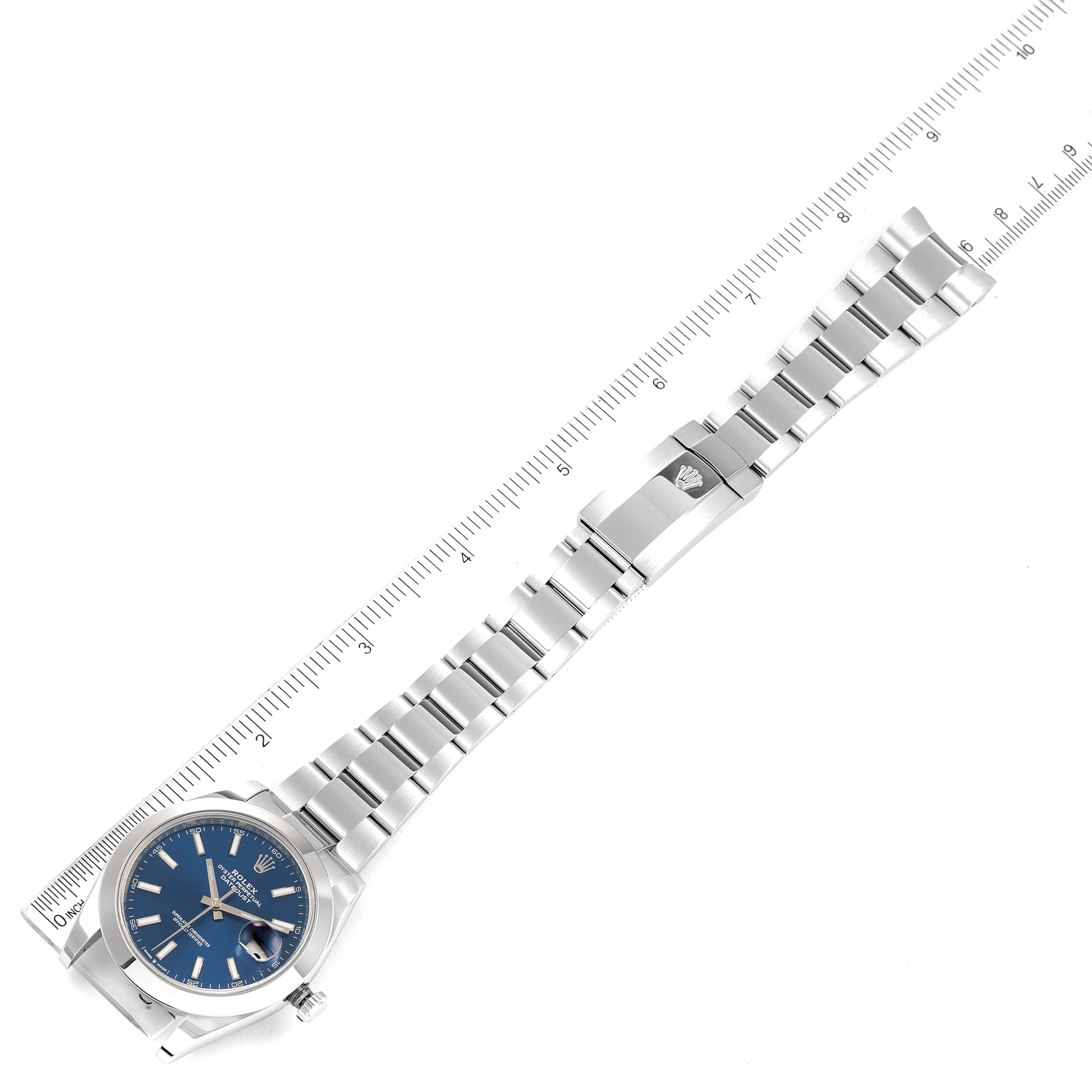The image shows a top view of a Rolex Datejust 41 126300 Men
s Stainless Steel Blue Dial 126300 Men
s Stainless Steel Blue Dial watch with a blue dial and a stainless steel bracelet placed alongside a ruler.