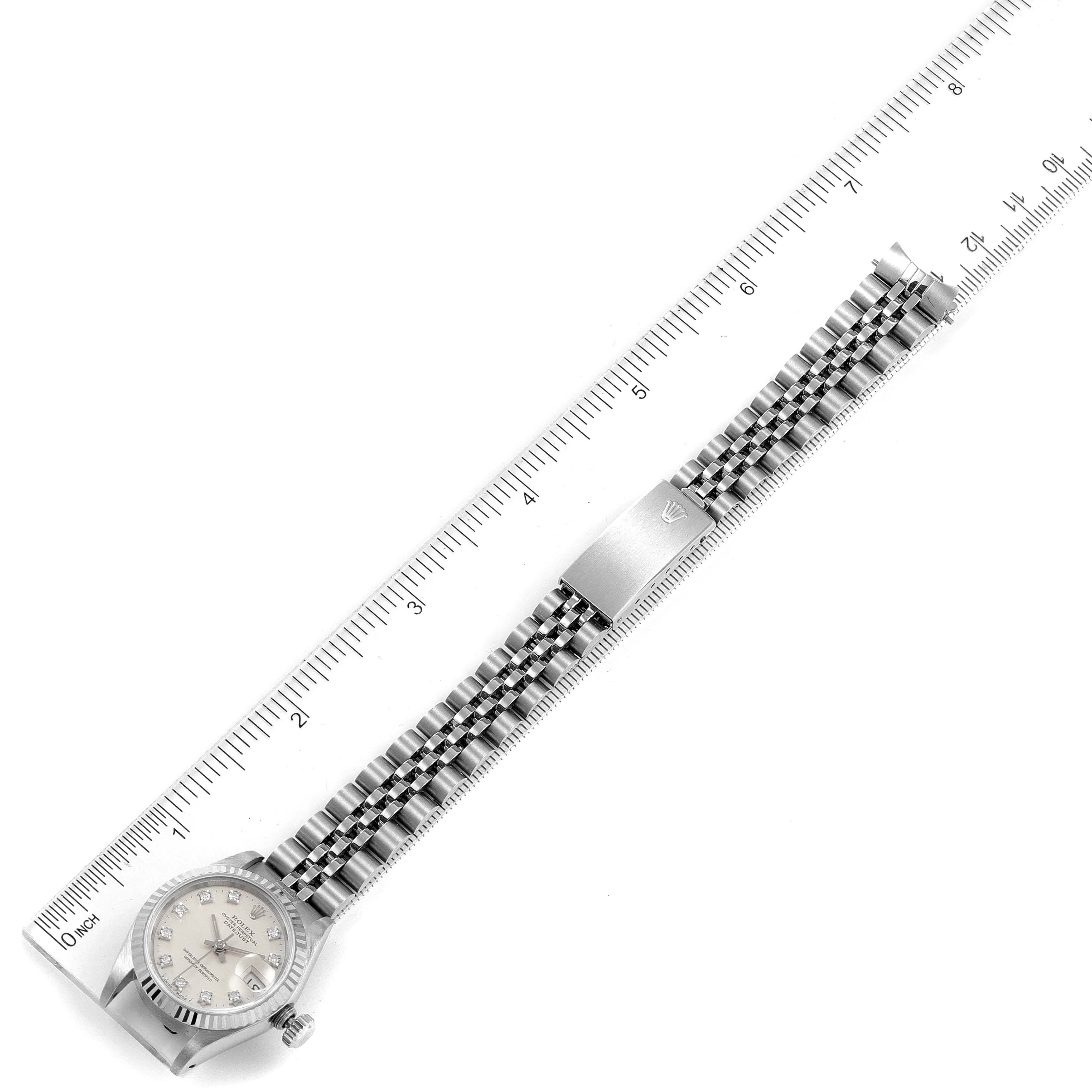 The Rolex Datejust 69174 Women
s Stainless Steel Silver Dial 69174 Women
s Stainless Steel Silver Dial watch is shown in a top-down angle, displaying its face, band, and a segment of a measuring ruler.