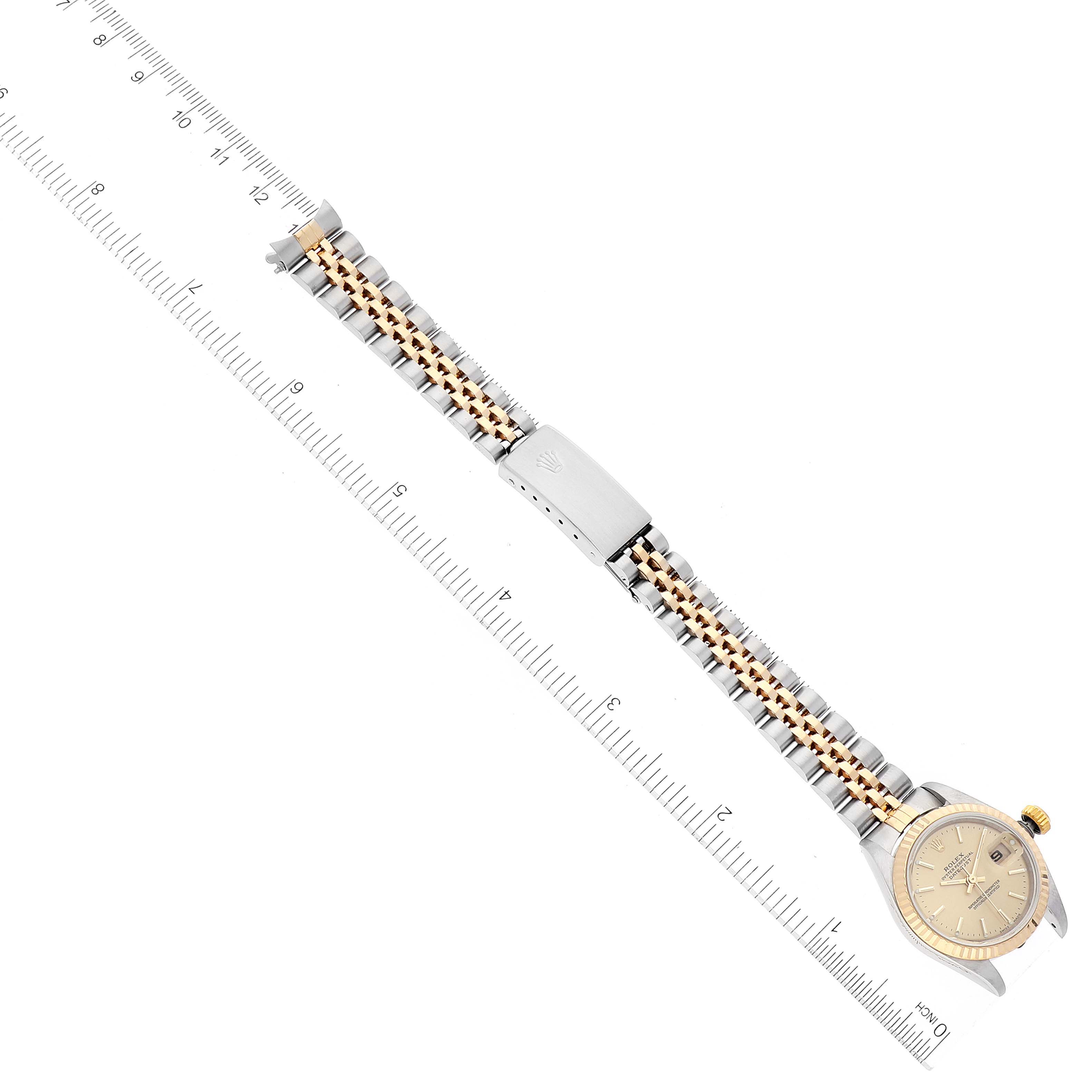 The image shows a top-down view of a Rolex Datejust 79173 Women's Steel and Gold (two tone) Champagne Dial 79173 Women's Steel and Gold (two tone) Champagne Dial watch, featuring its bracelet and dial alongside a ruler for scale.