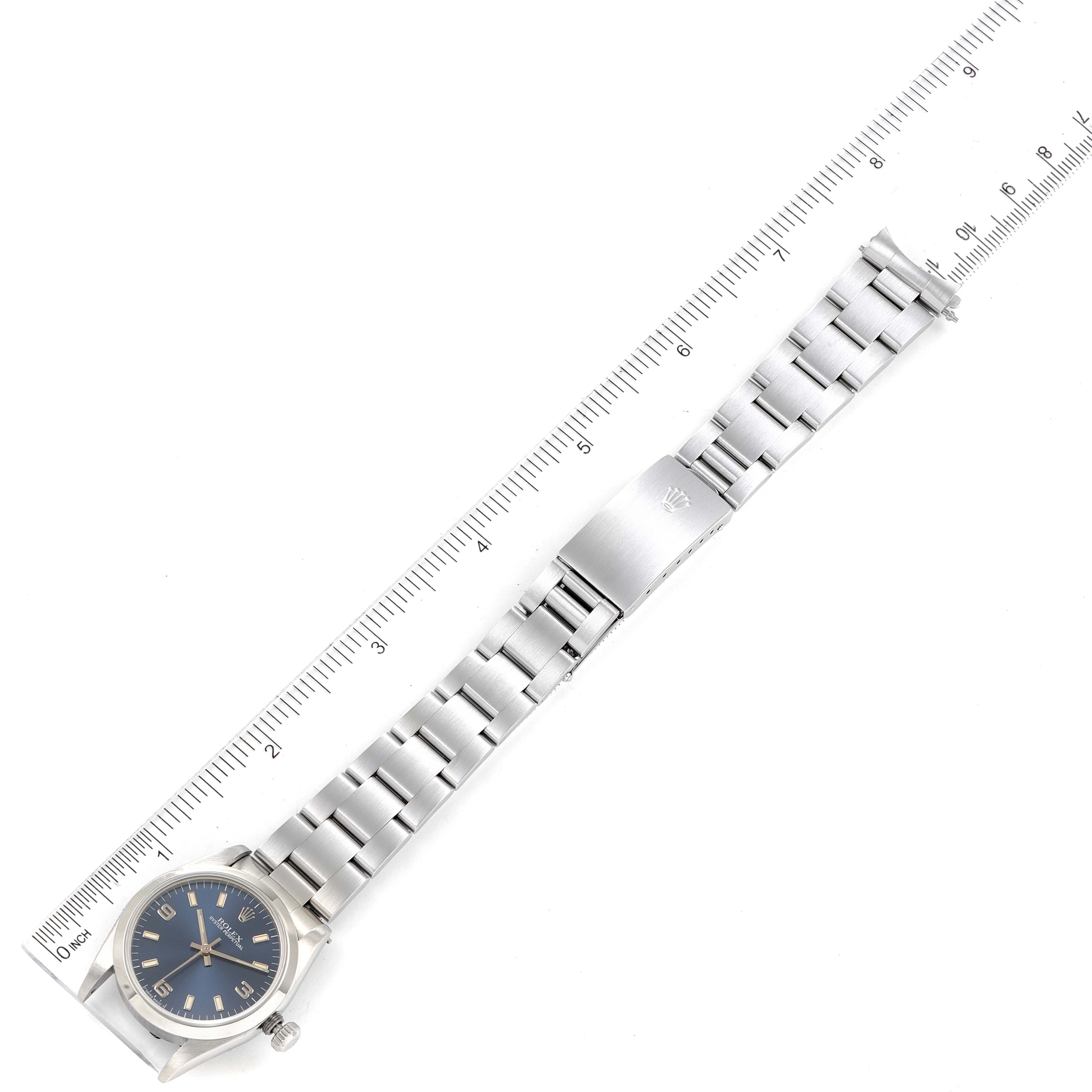 The image shows a top-down view of a Rolex Mid-Size 67480 Women
s Stainless Steel Blue Dial 67480 Women
s Stainless Steel Blue Dial model watch with a blue dial and silver bracelet next to a ruler for scale.