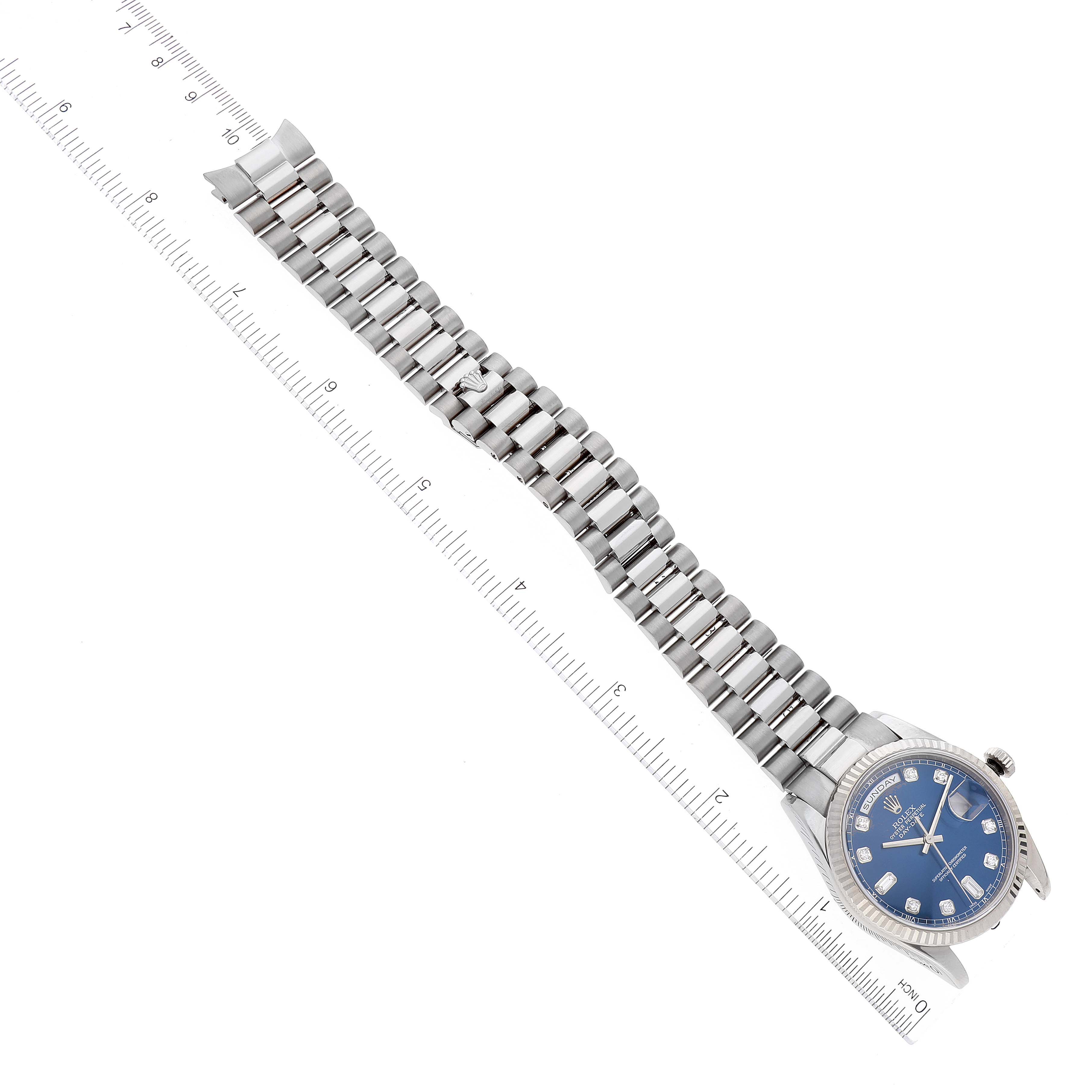 The image shows a top-view angle of a Rolex President 118239 Men's White Gold Blue Dial 118239 Men's White Gold Blue Dial model watch with a blue dial and its metal bracelet laid alongside a ruler.