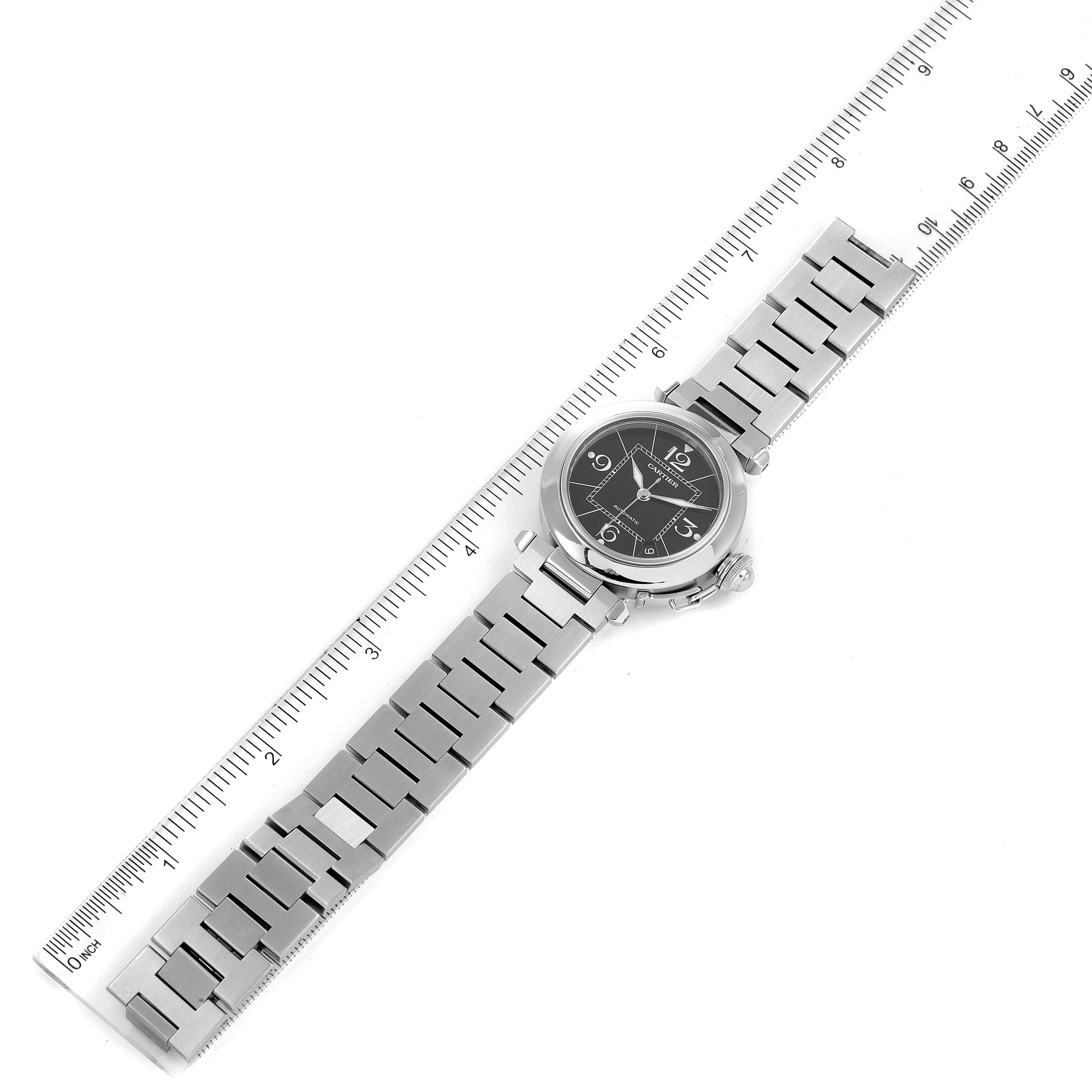 The Cartier Pasha W31076M7 Men's Stainless Steel Black Dial W31076M7 Men's Stainless Steel Black Dial watch is shown from an overhead angle, displaying the face, metal strap, and side crown, with a ruler for scale.