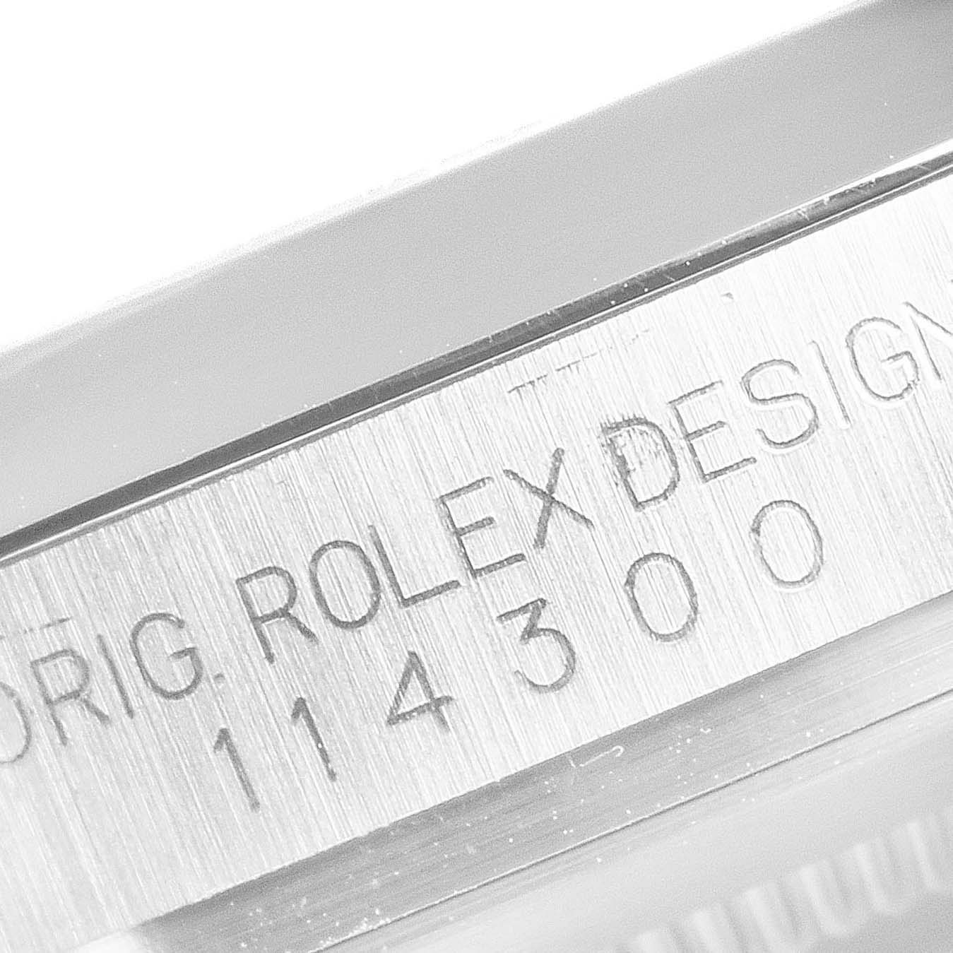 The image shows a close-up of the engraved serial number on the casing of a Rolex Oyster Perpetual 114300 Men's Stainless Steel Silver Dial 114300 Men's Stainless Steel Silver Dial model.