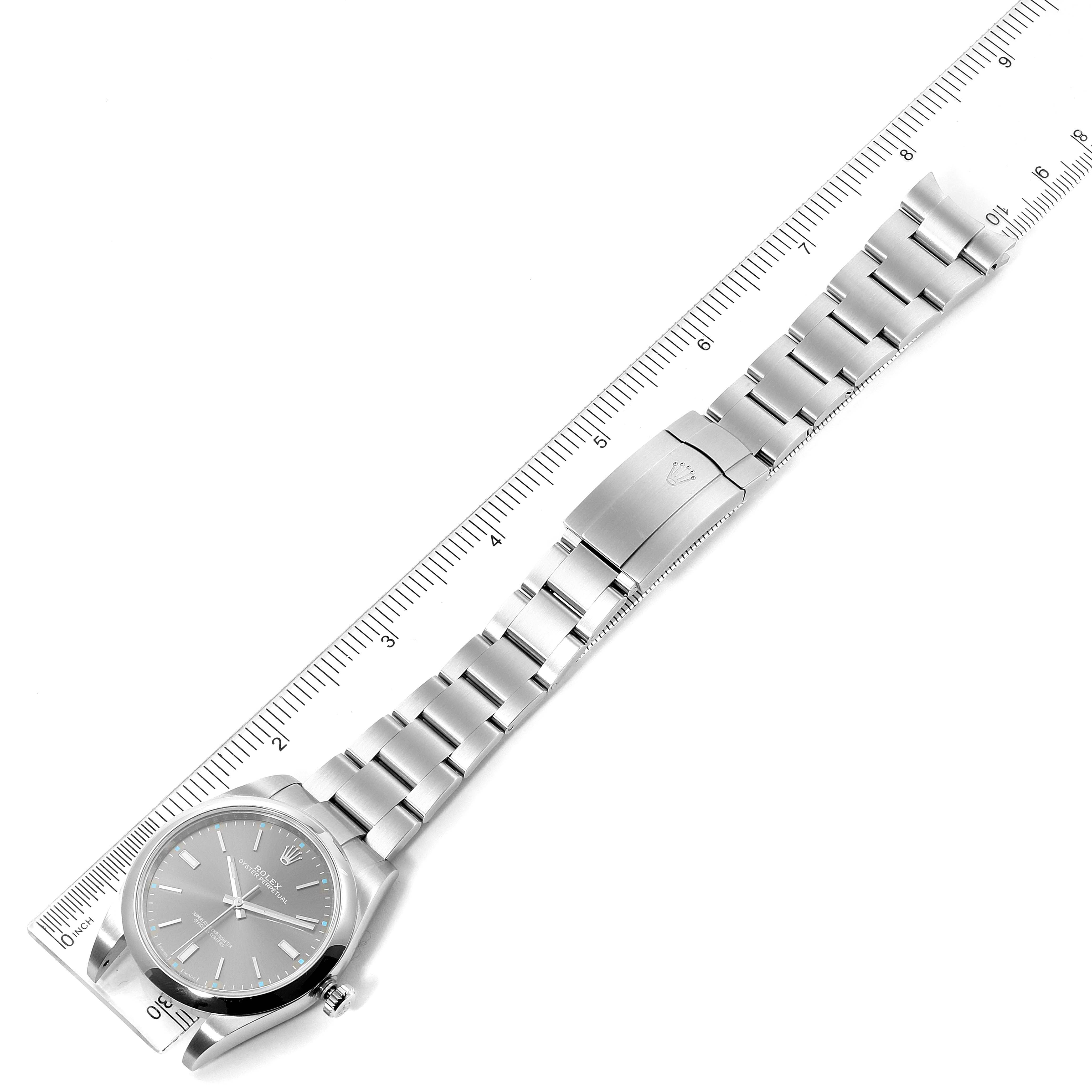 The image shows a top-down view of a Rolex Oyster Perpetual 114300 Men's Stainless Steel Silver Dial 114300 Men's Stainless Steel Silver Dial watch with its dial, bracelet, and clasp visible alongside a ruler for scale.