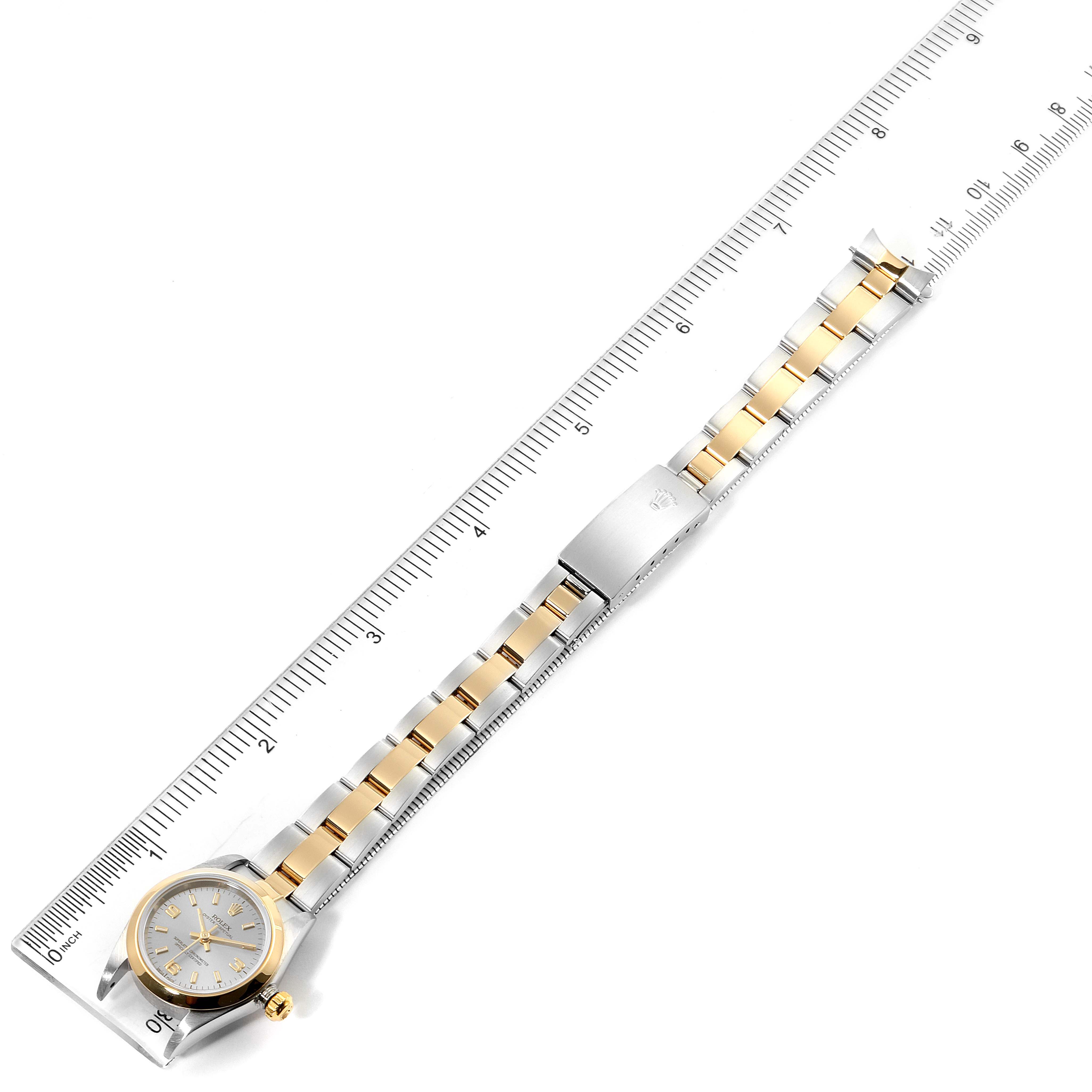 The Rolex Oyster Perpetual 76183 Women's Steel and Gold (two tone) Grey Dial 76183 Women's Steel and Gold (two tone) Grey Dial watch is shown from a top-down angle, displaying its face, bracelet, and clasp alongside a ruler.