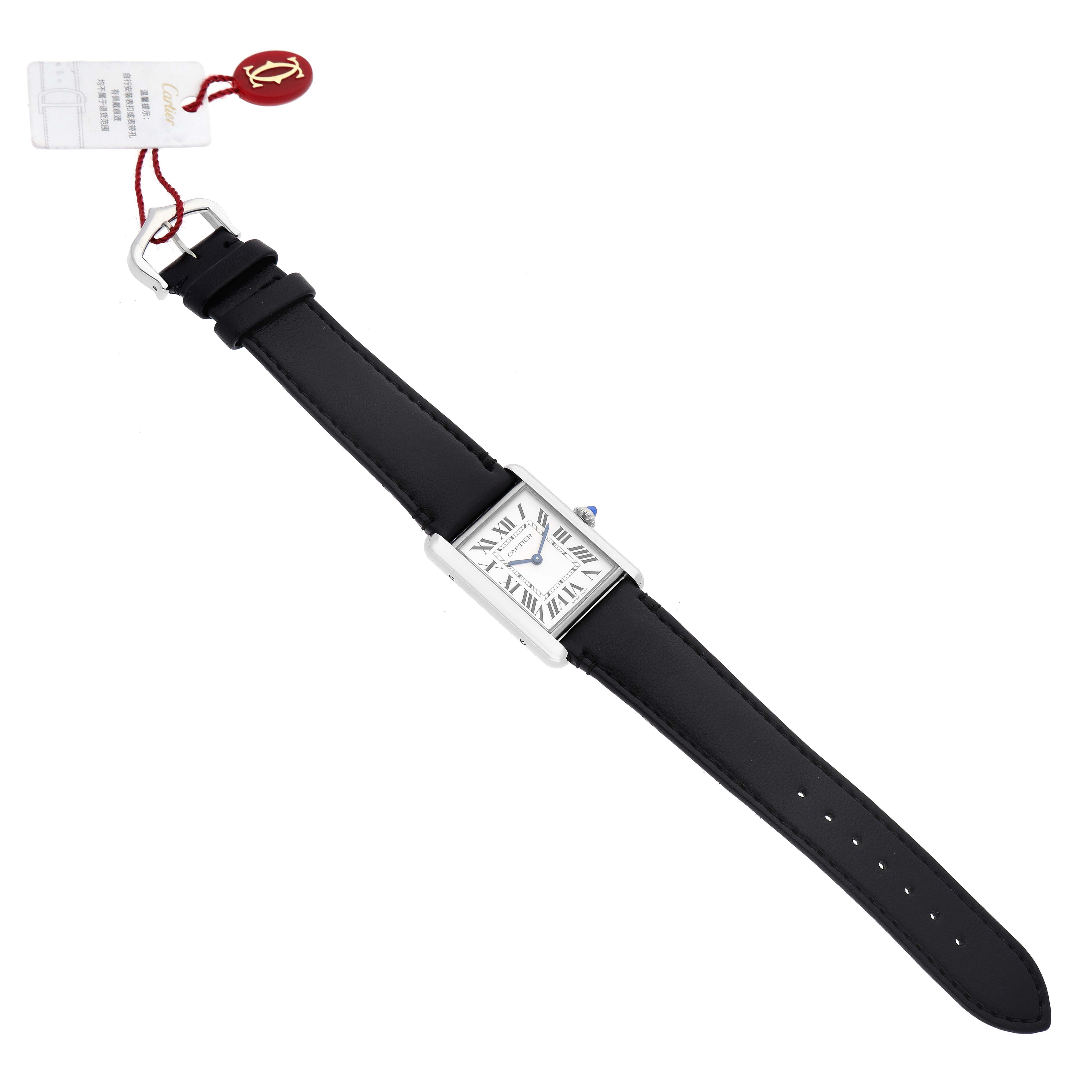 The image shows a full view of the Cartier Tank Must WSTA0059 Women's Stainless Steel Silver Dial WSTA0059 Women's Stainless Steel Silver Dial watch laid flat, showcasing the face, strap, and attached tag.