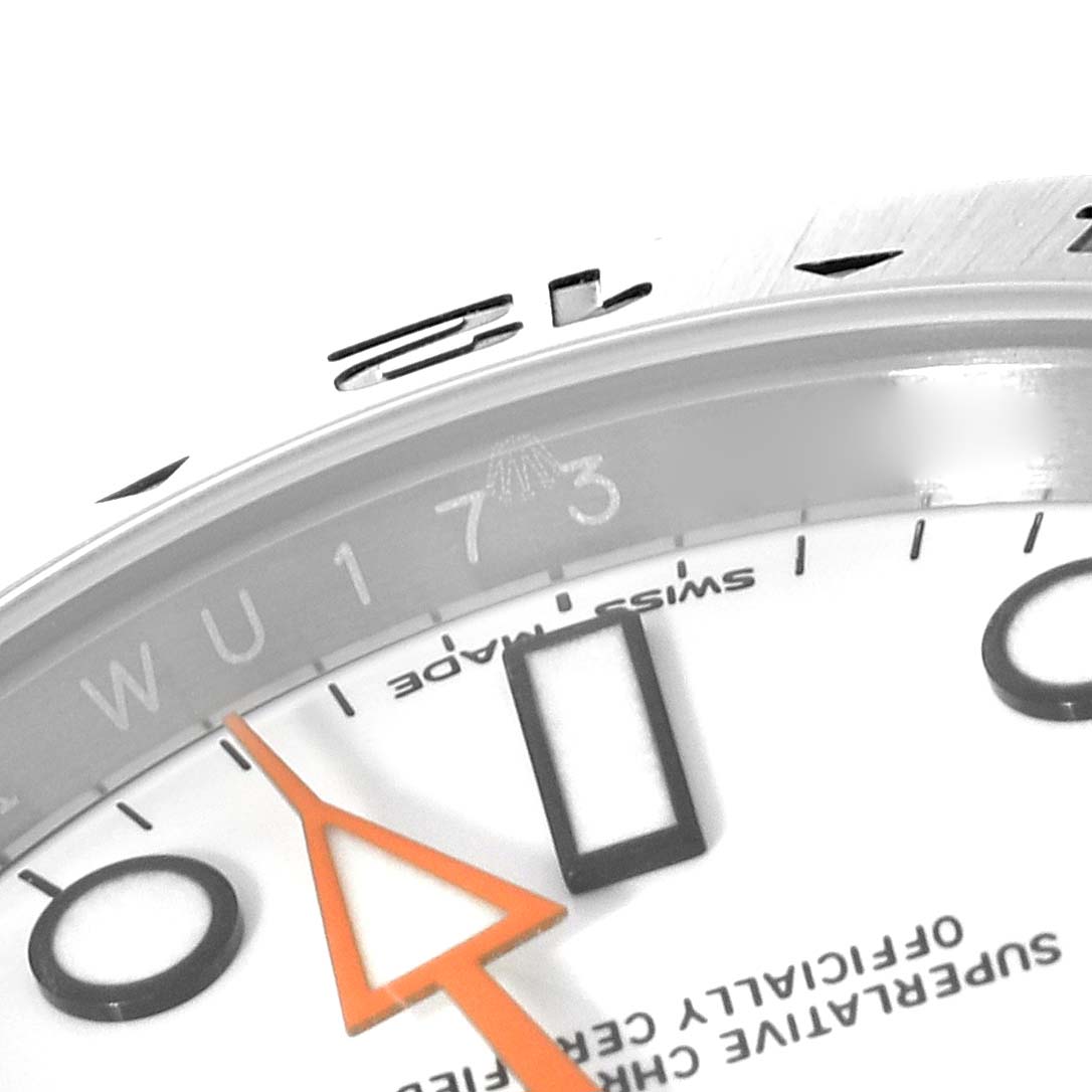 The image shows a close-up angle of the Rolex Explorer 216570 Men's Stainless Steel White Dial 216570 Men's Stainless Steel White Dial watch's dial and part of its orange hand, focusing on the date and text.