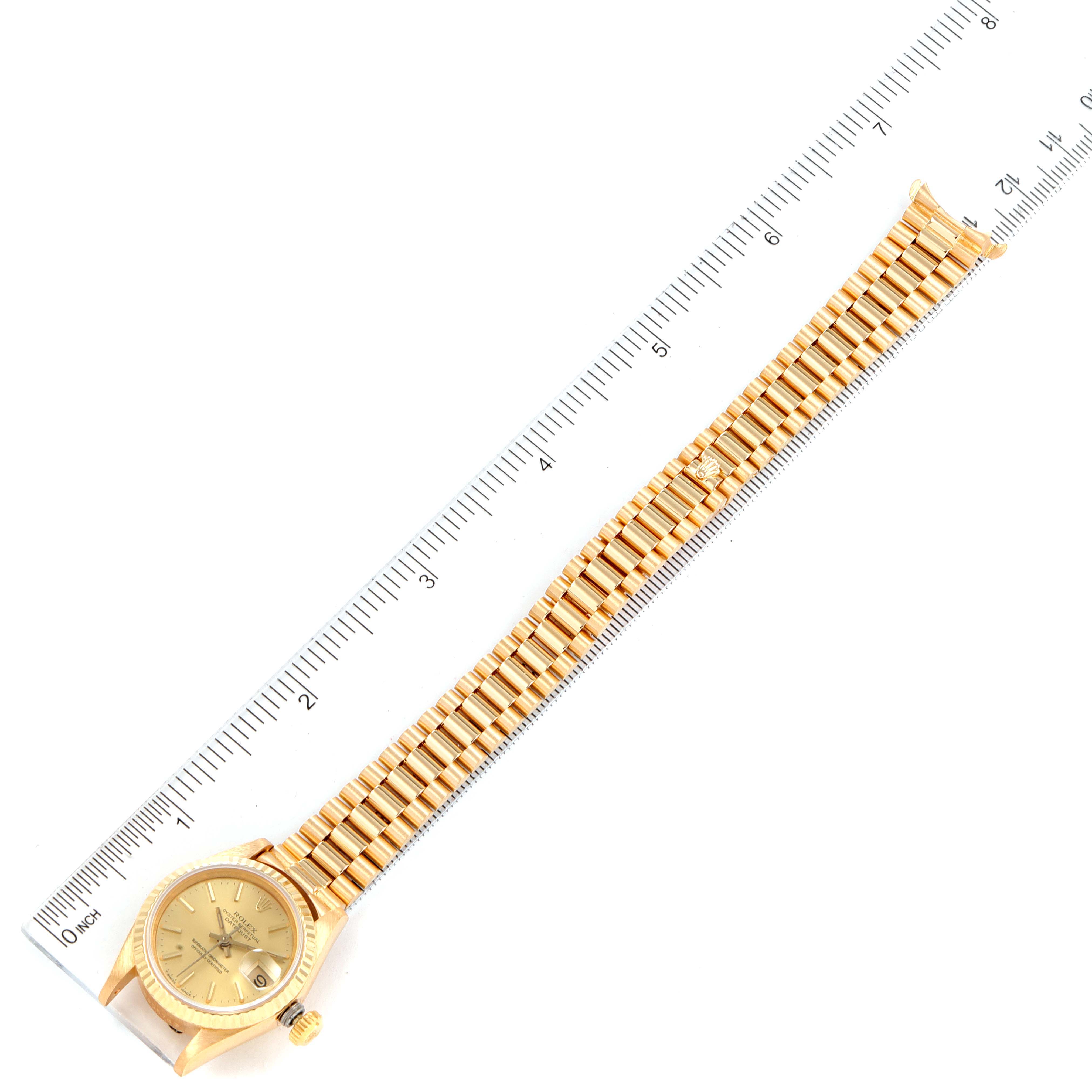 The image shows a top-down view of a Rolex President 69178 Women's Yellow Gold Champagne Dial 69178 Women's Yellow Gold Champagne Dial model watch with its full length and bracelet displayed alongside a ruler.