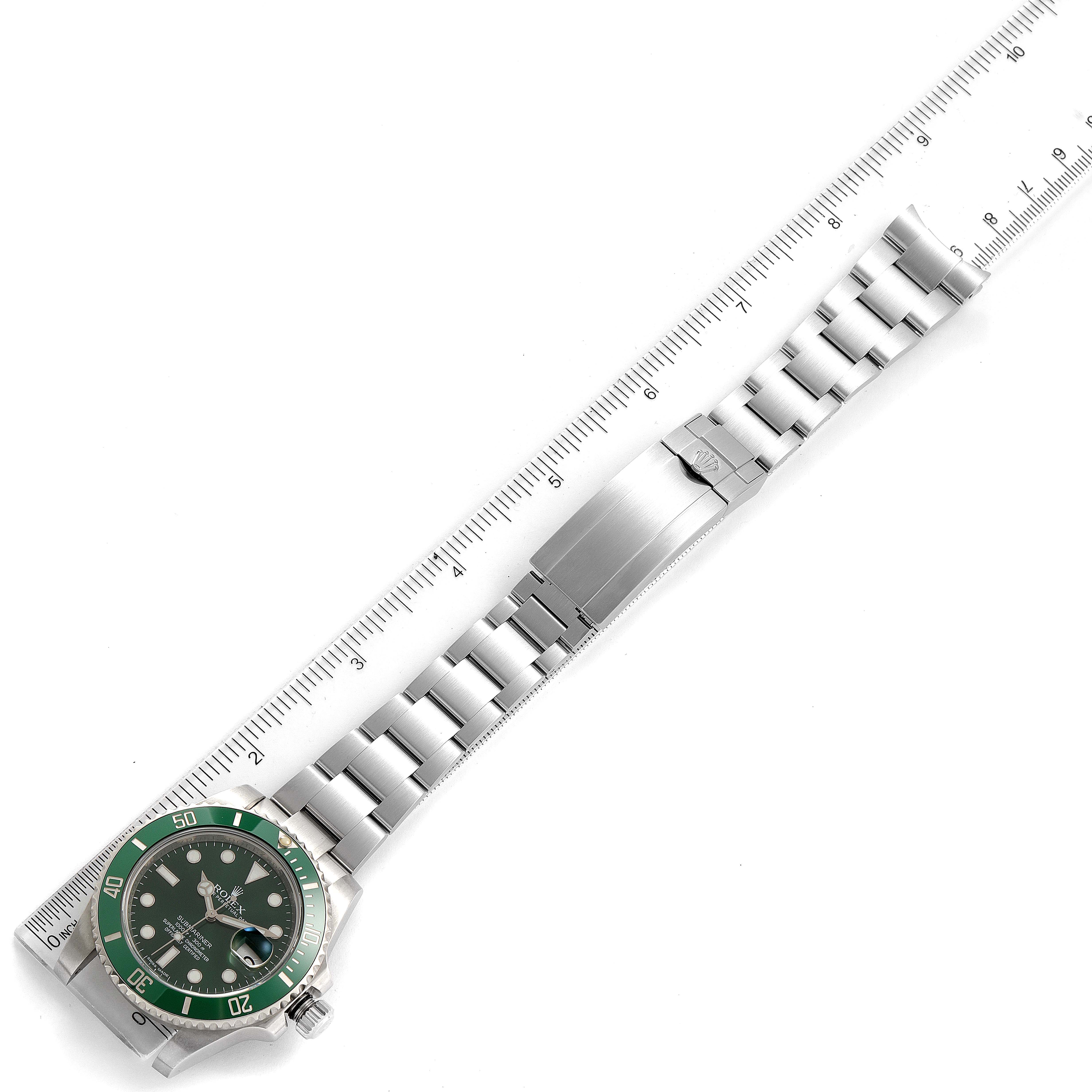 This image shows a top-down view of a Rolex Submariner 116610LV Men's Stainless Steel Green Dial 116610LV Men's Stainless Steel Green Dial watch lying flat with an extended metal bracelet adjacent to a ruler.